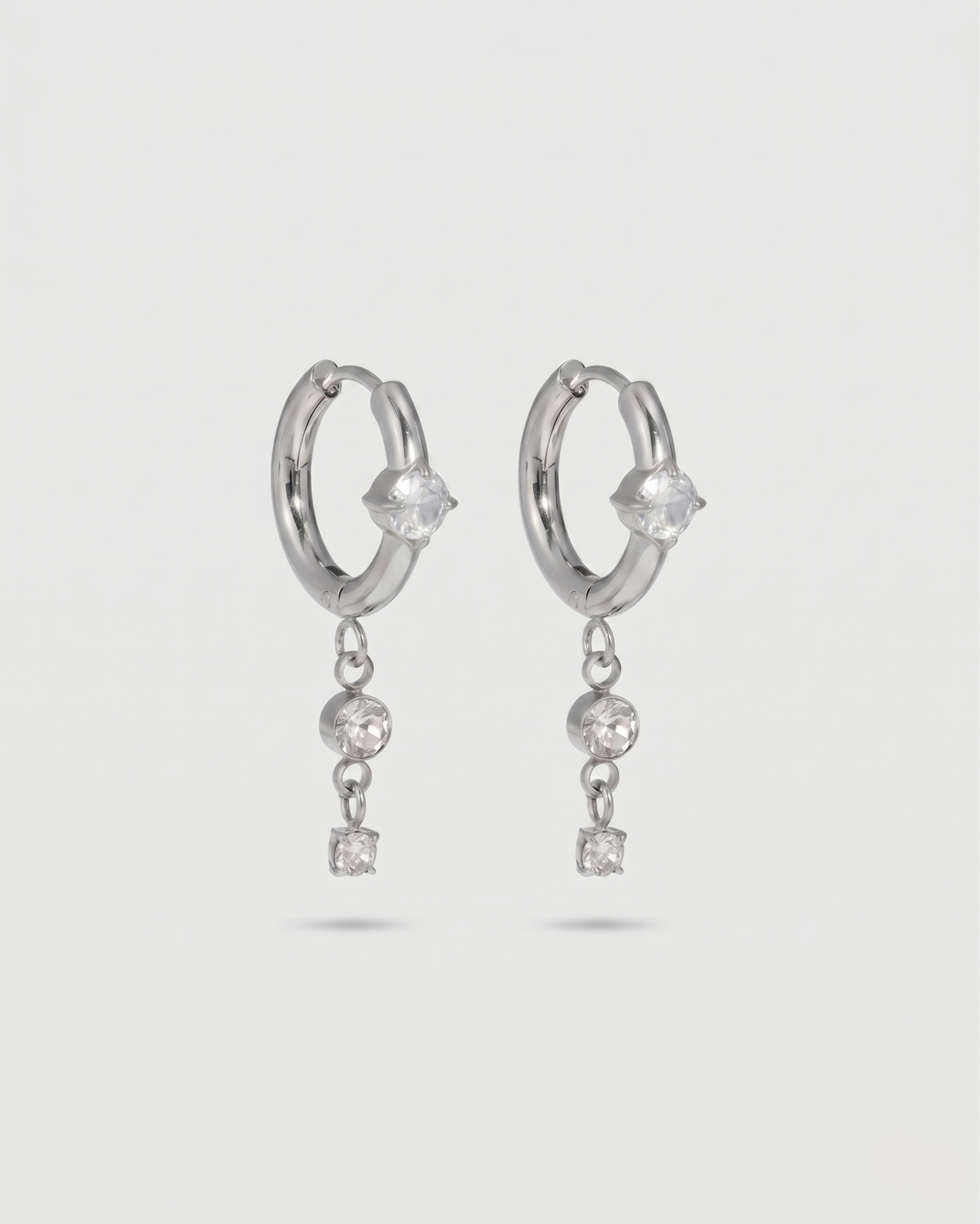 Silver hoop earrings with dangling crystals on a light gray background