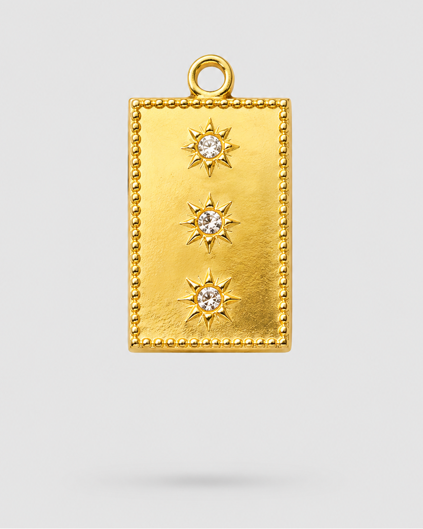 A gold rectangular pendant charm with a beaded border, three vertical rows of starburst motifs, and a clear central gemstone in each star, shown on a light gray background.