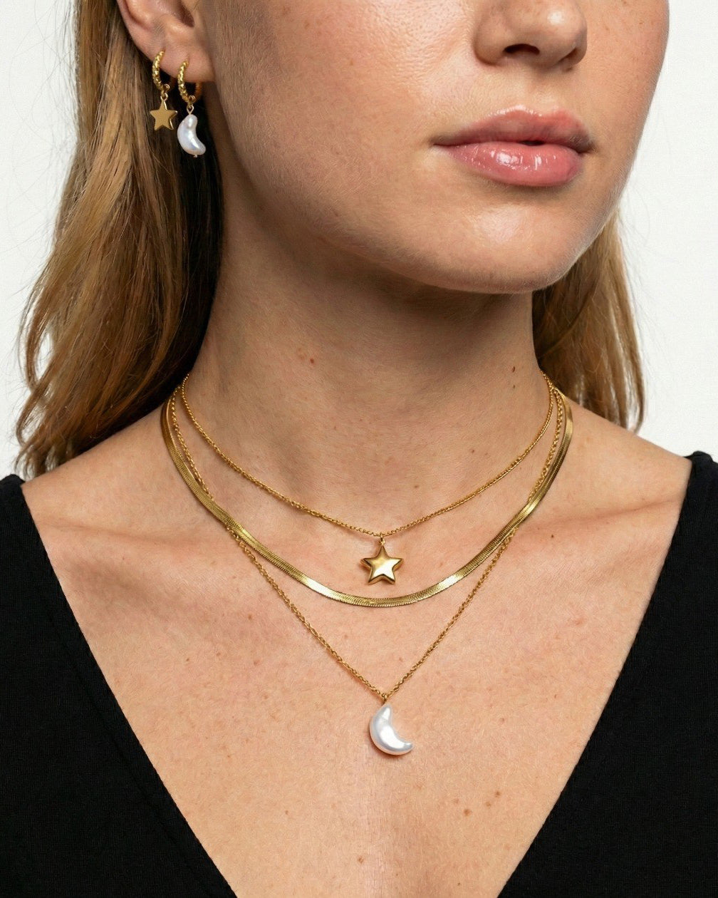 Close-up of a person wearing gold necklaces with star and moon pendants on a plain background