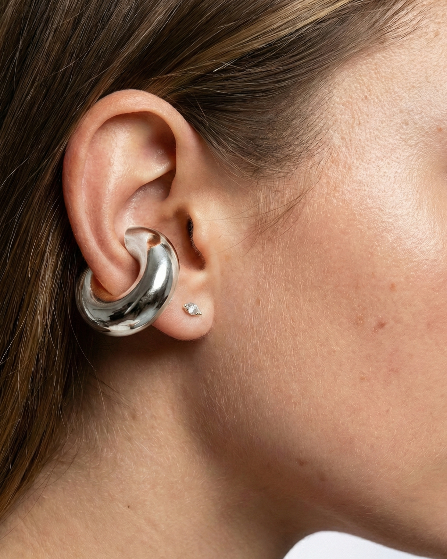 Close-up of an ear wearing a silver hoop earring with a blurred background