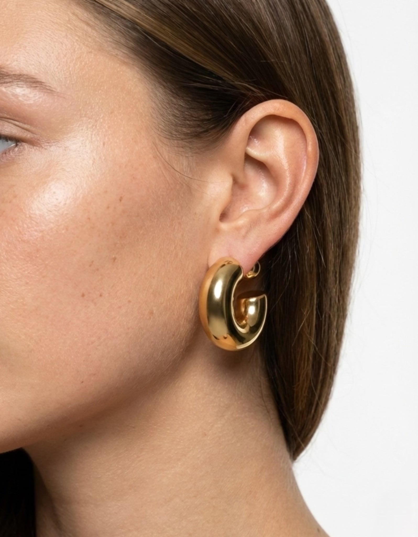 Close-up of a person wearing a gold hoop earring on a neutral background