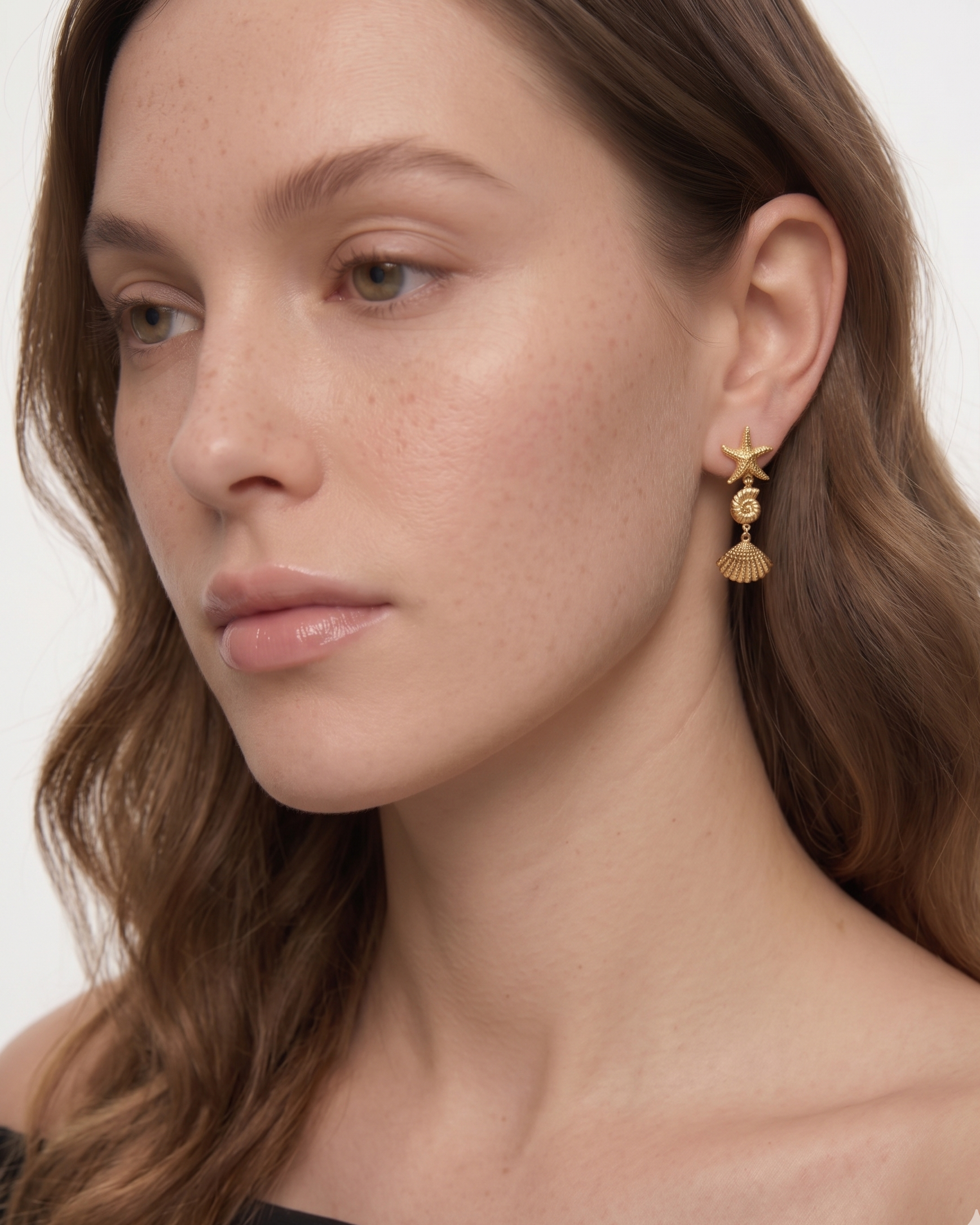 Close-up of a woman wearing gold starfish earrings on a white background