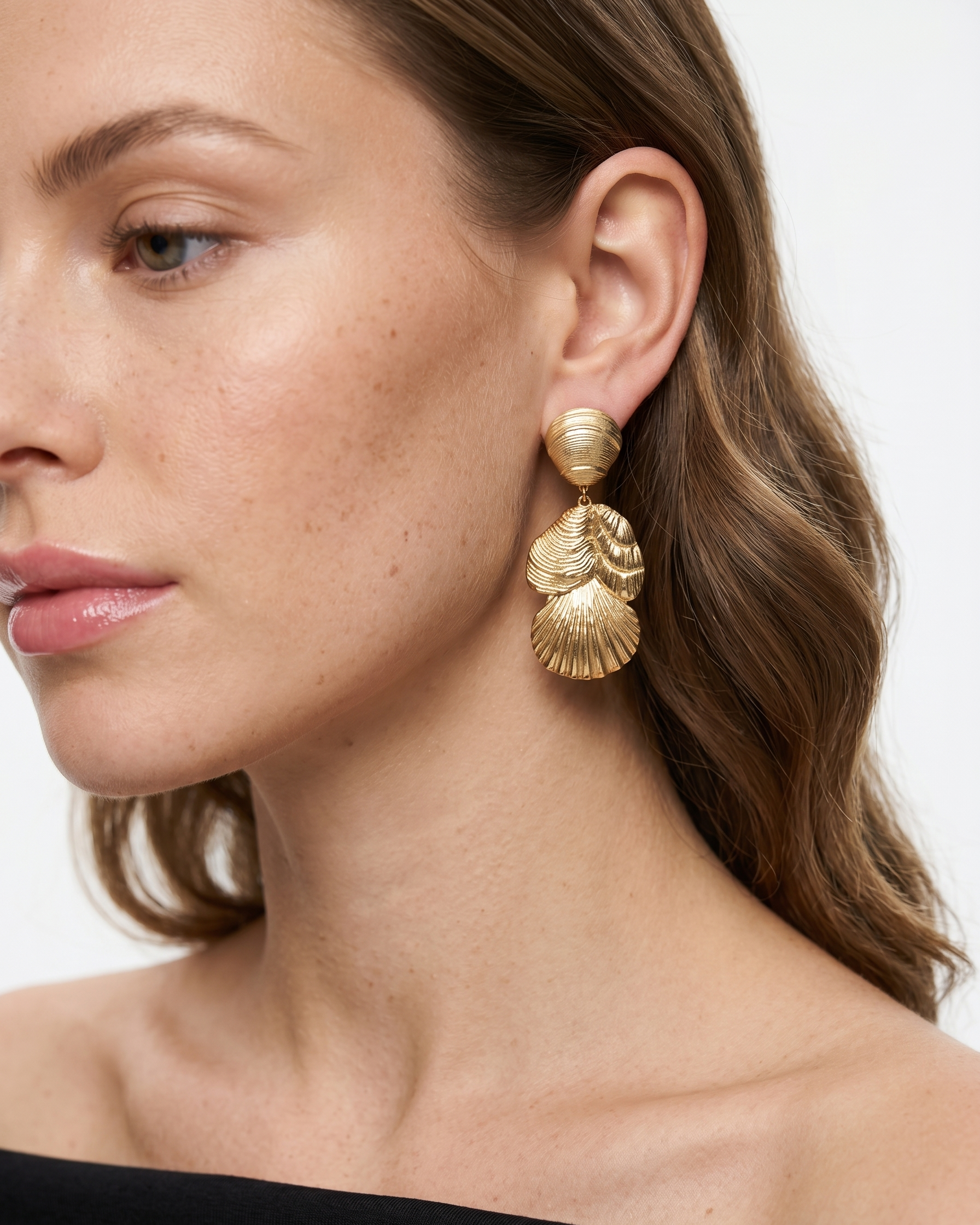 Woman wearing gold leaf-shaped earrings on a white background