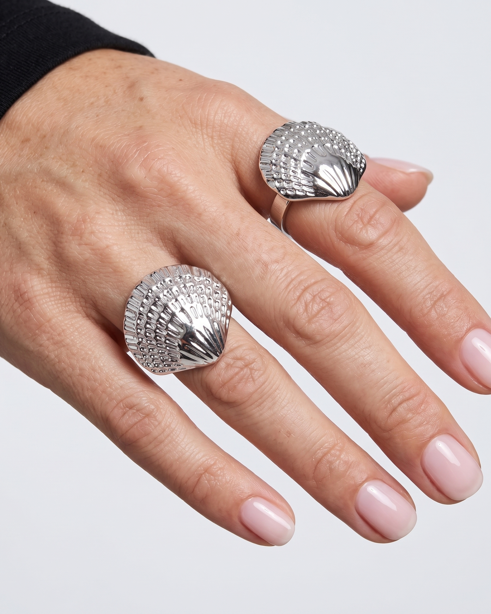 Hand wearing two silver shell-shaped rings on a light gray background