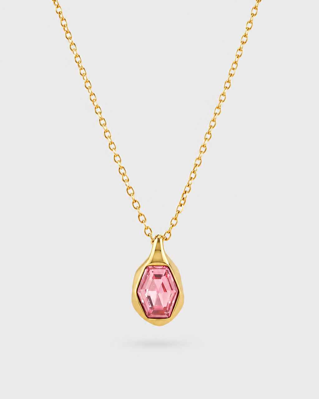 A gold chain necklace with a teardrop-shaped pendant featuring a faceted pink gemstone in a gold bezel setting, shown against a light gray background.