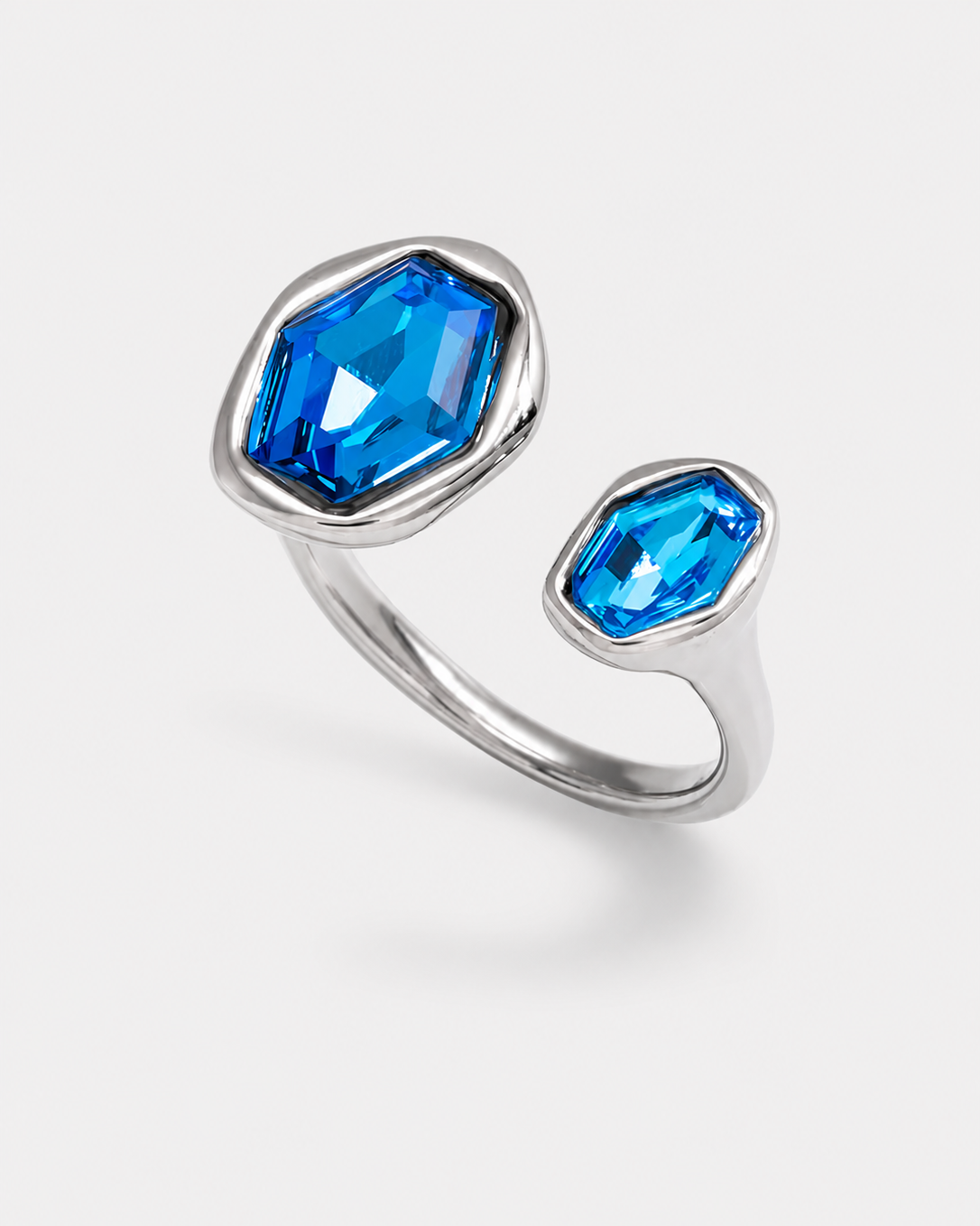 A silver-toned ring featuring two bezel-set blue gemstones of different sizes on a light gray background.