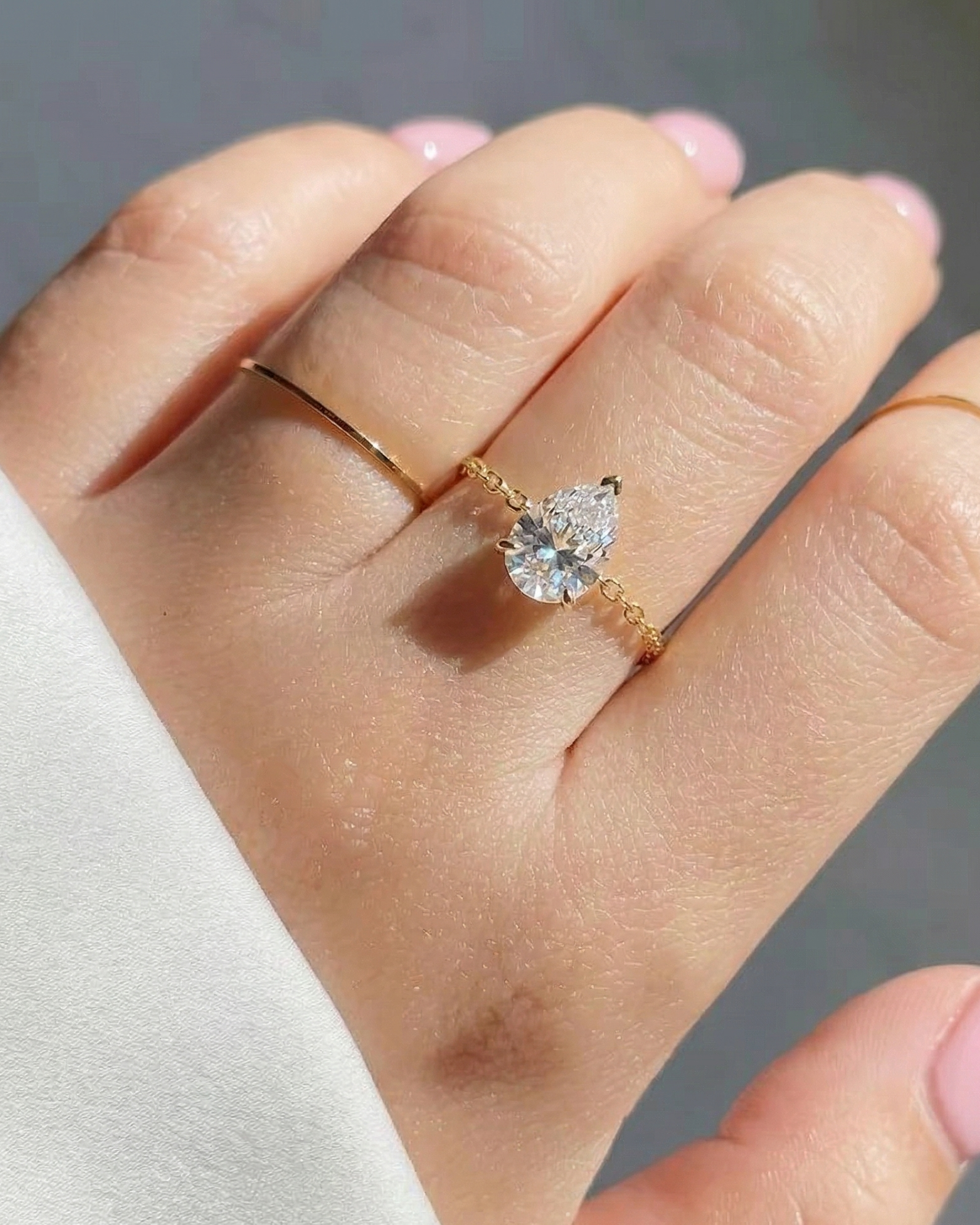 Hand wearing a gold ring with a heart-shaped diamond on a neutral background