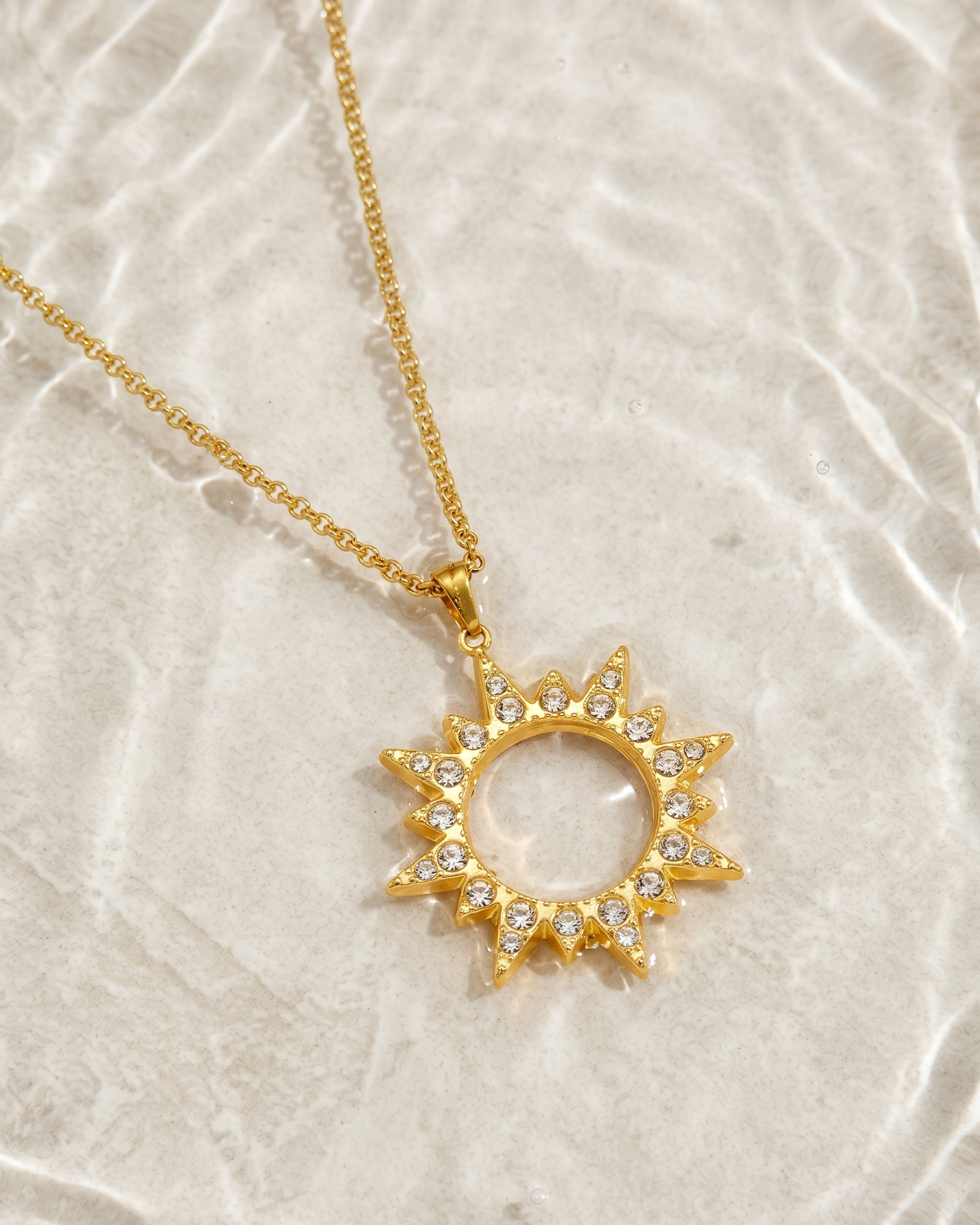 Gold necklace with a sun-shaped pendant on a textured beige background
