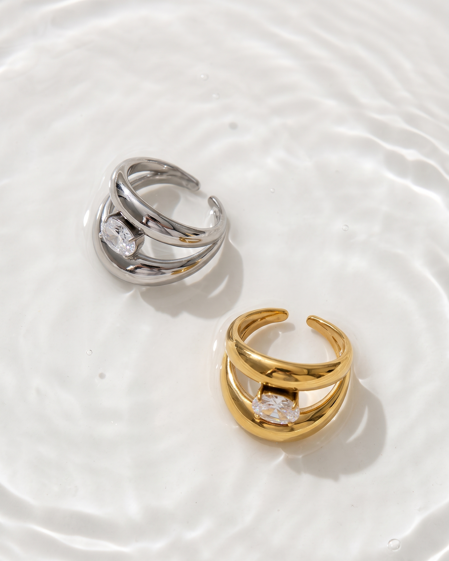Two rings, one gold and one silver, on a white surface with water effect