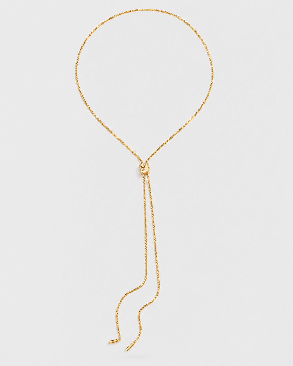 A gold chain lariat necklace with a knotted center and long dangling tails, displayed on a light gray background.