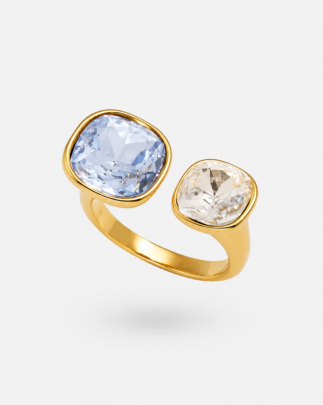 A gold ring with two cushion-cut gemstones, one light blue and one clear, set against a light gray background.