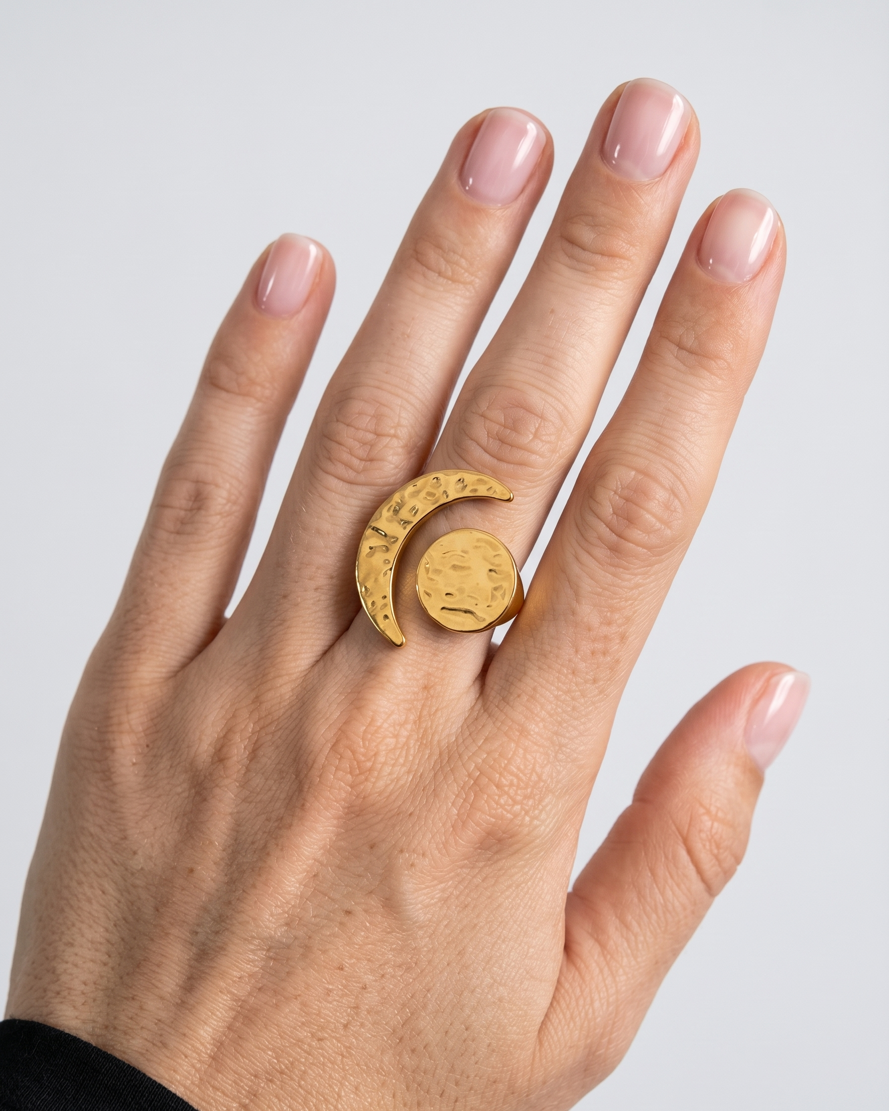 Hand wearing a gold ring with a moon design on a light gray background