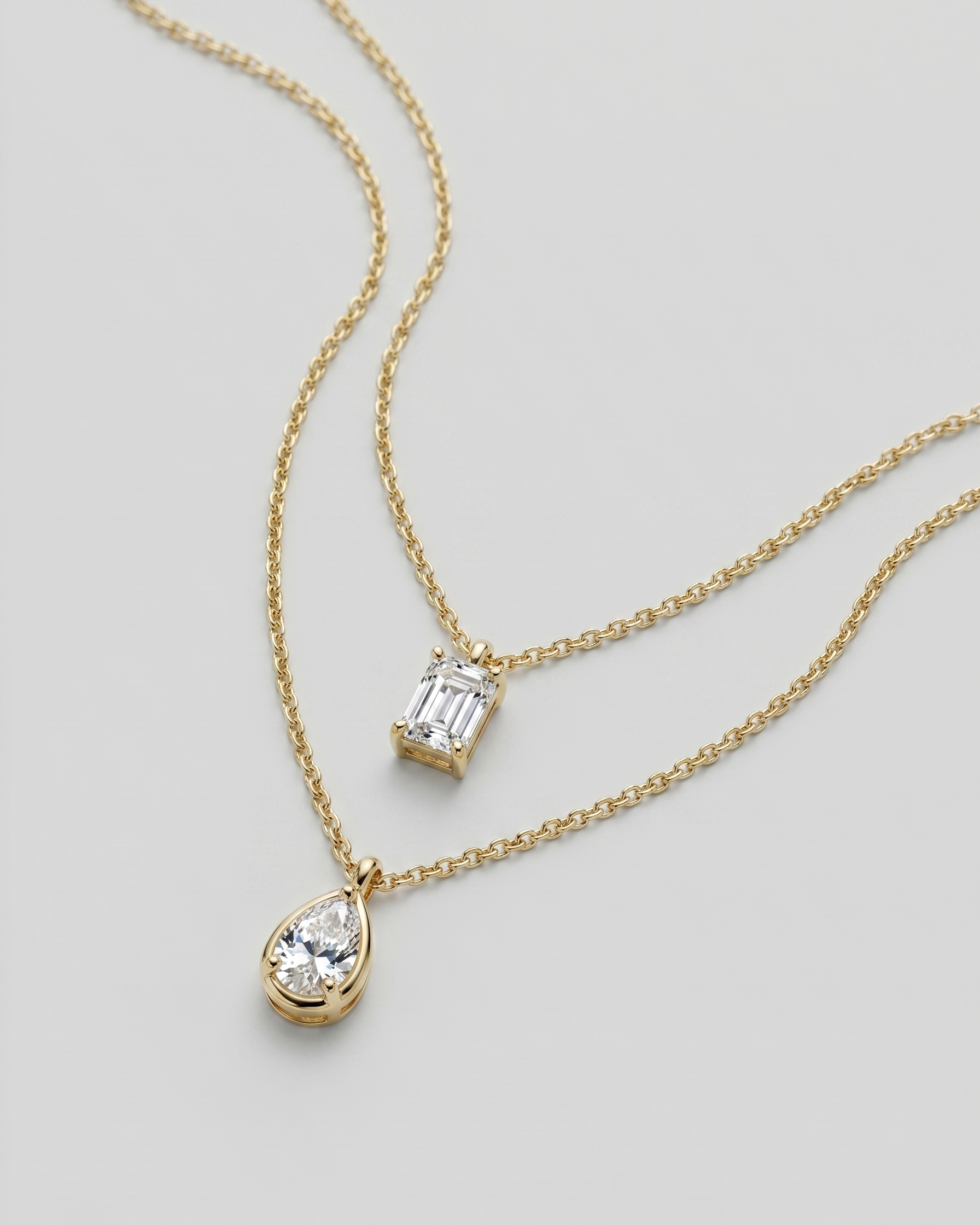 Two gold necklaces with diamond pendants on a light gray background