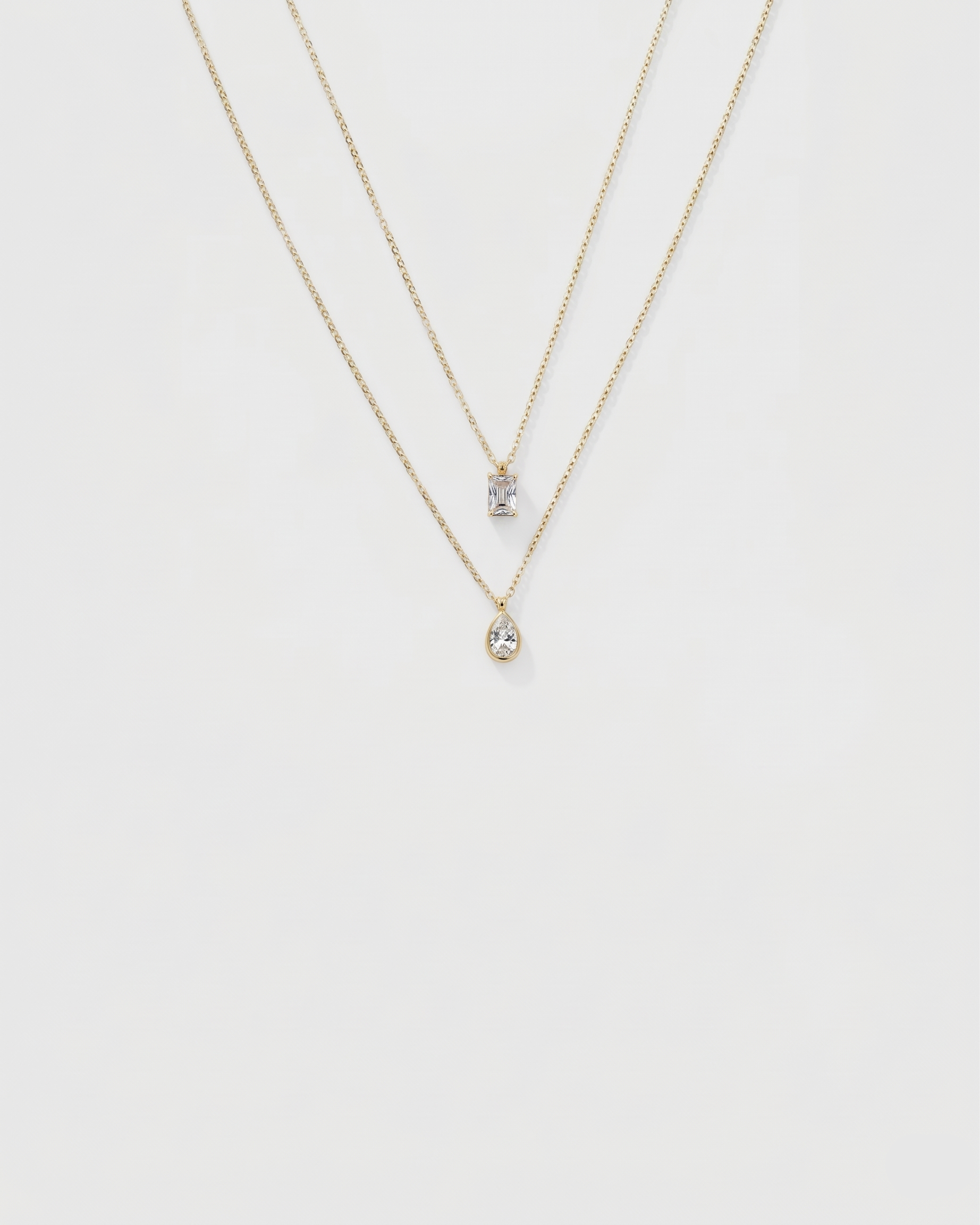 Two gold necklaces with small pendants on a white background