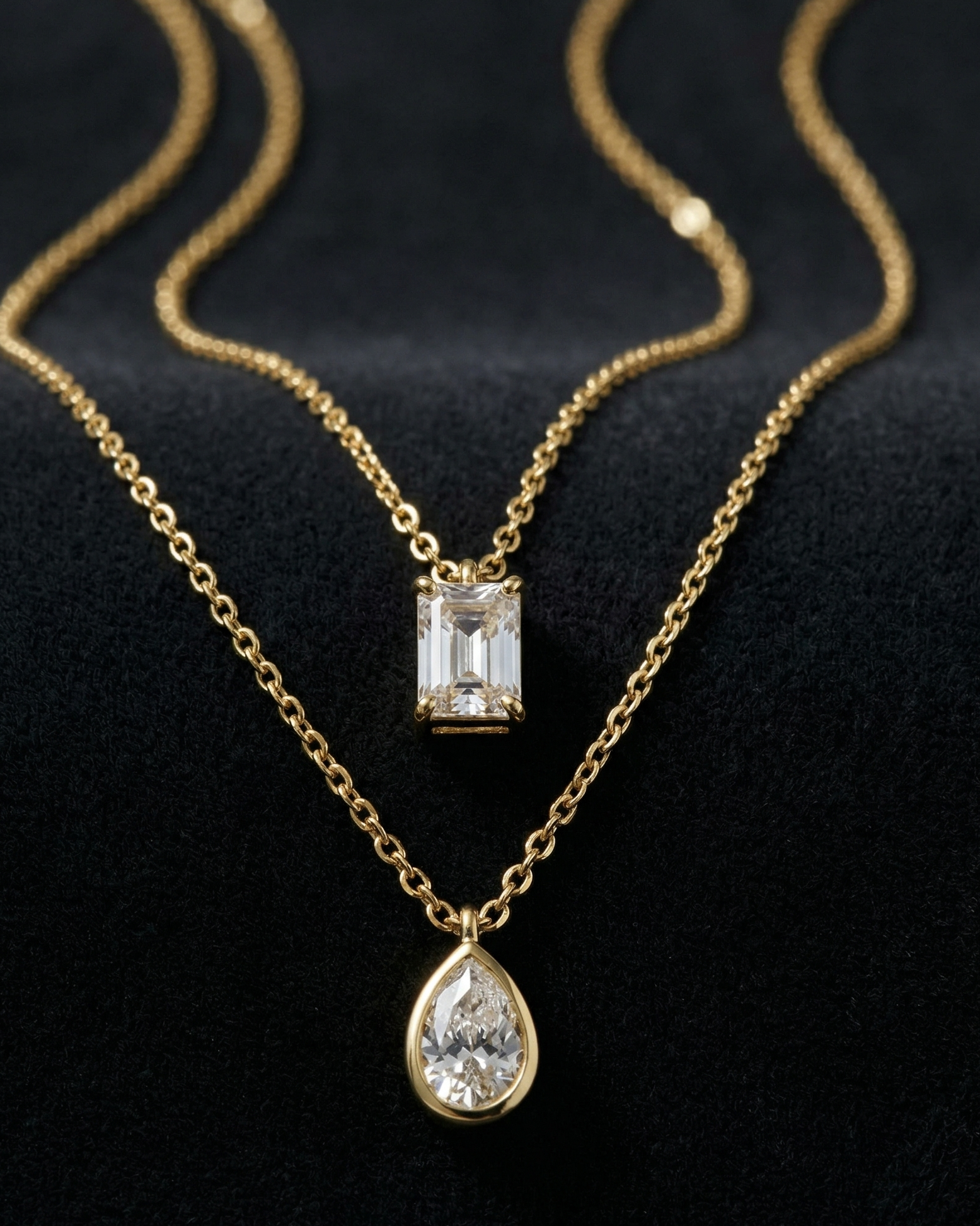 Two gold necklaces with diamond pendants on a black background