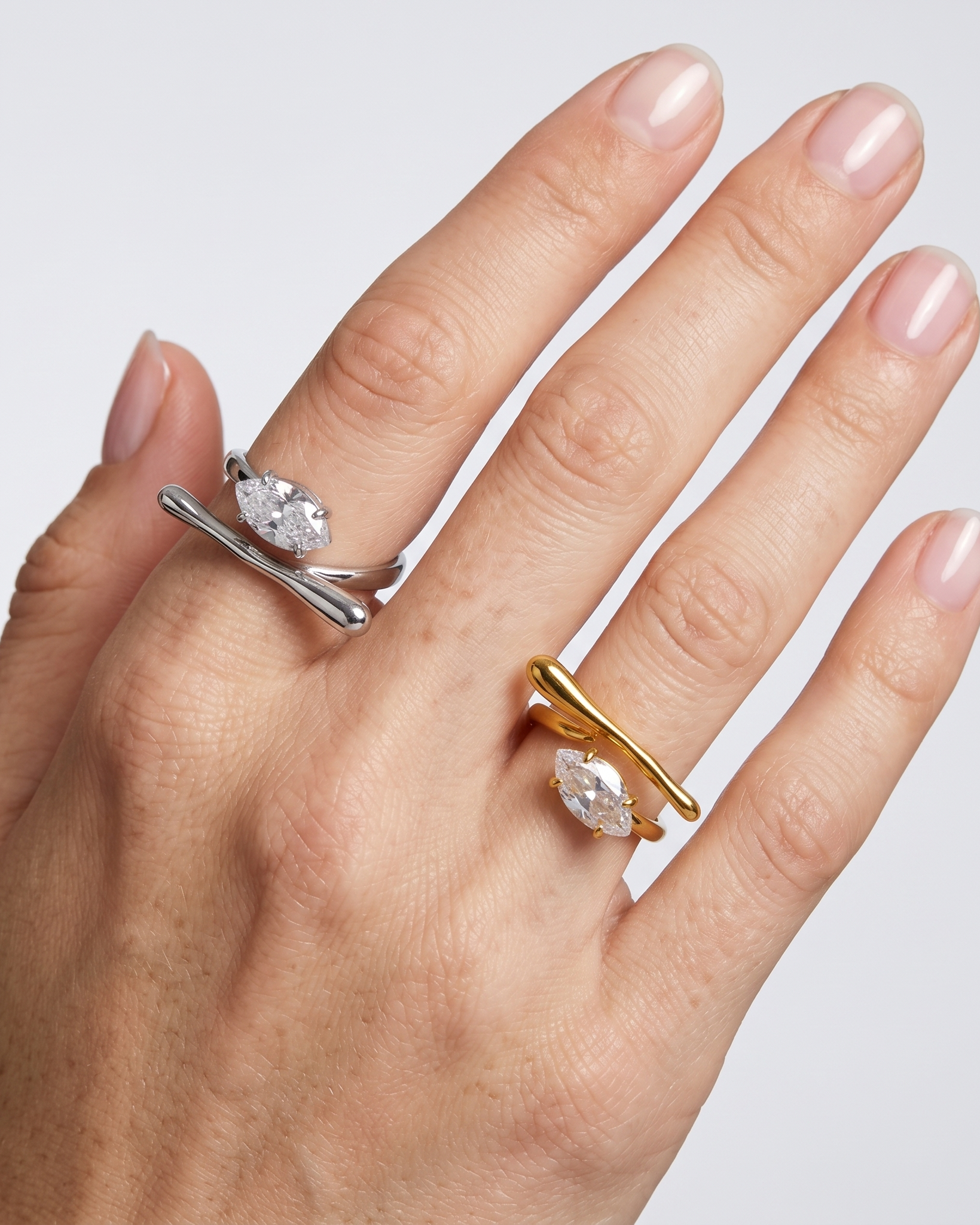 Hand wearing two rings with diamond accents on a light gray background