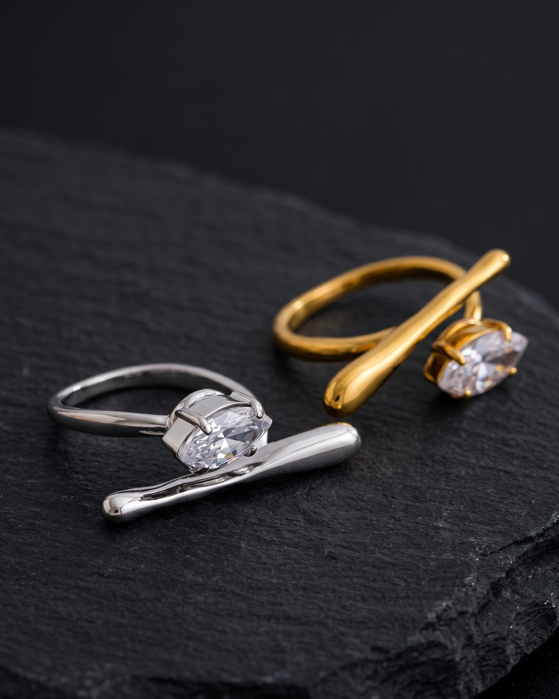 Two rings, one silver and one gold, on a dark surface.