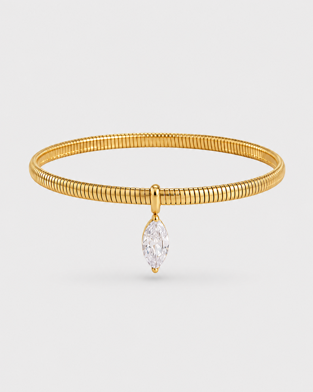 A gold snake-bone bangle bracelet featuring a dangling marquise-cut clear gemstone, presented on a light gray background.