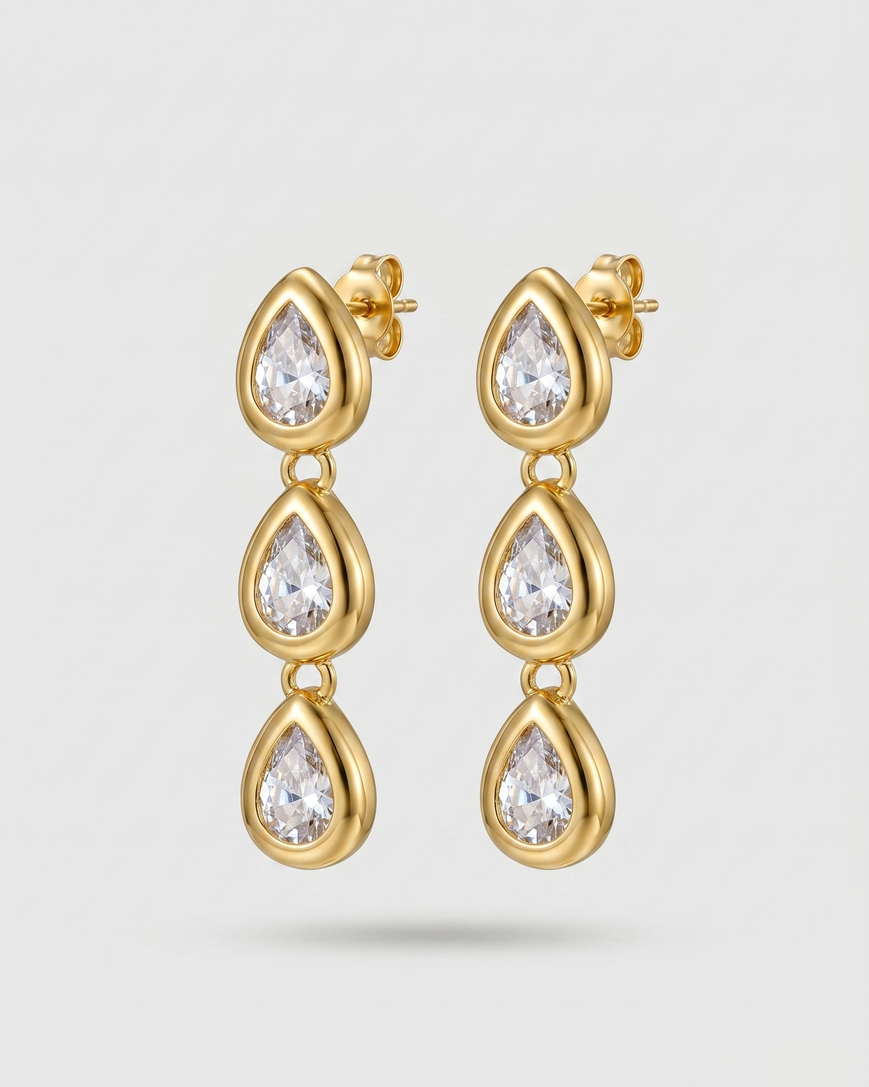 Gold earrings with clear gemstones on a light gray background