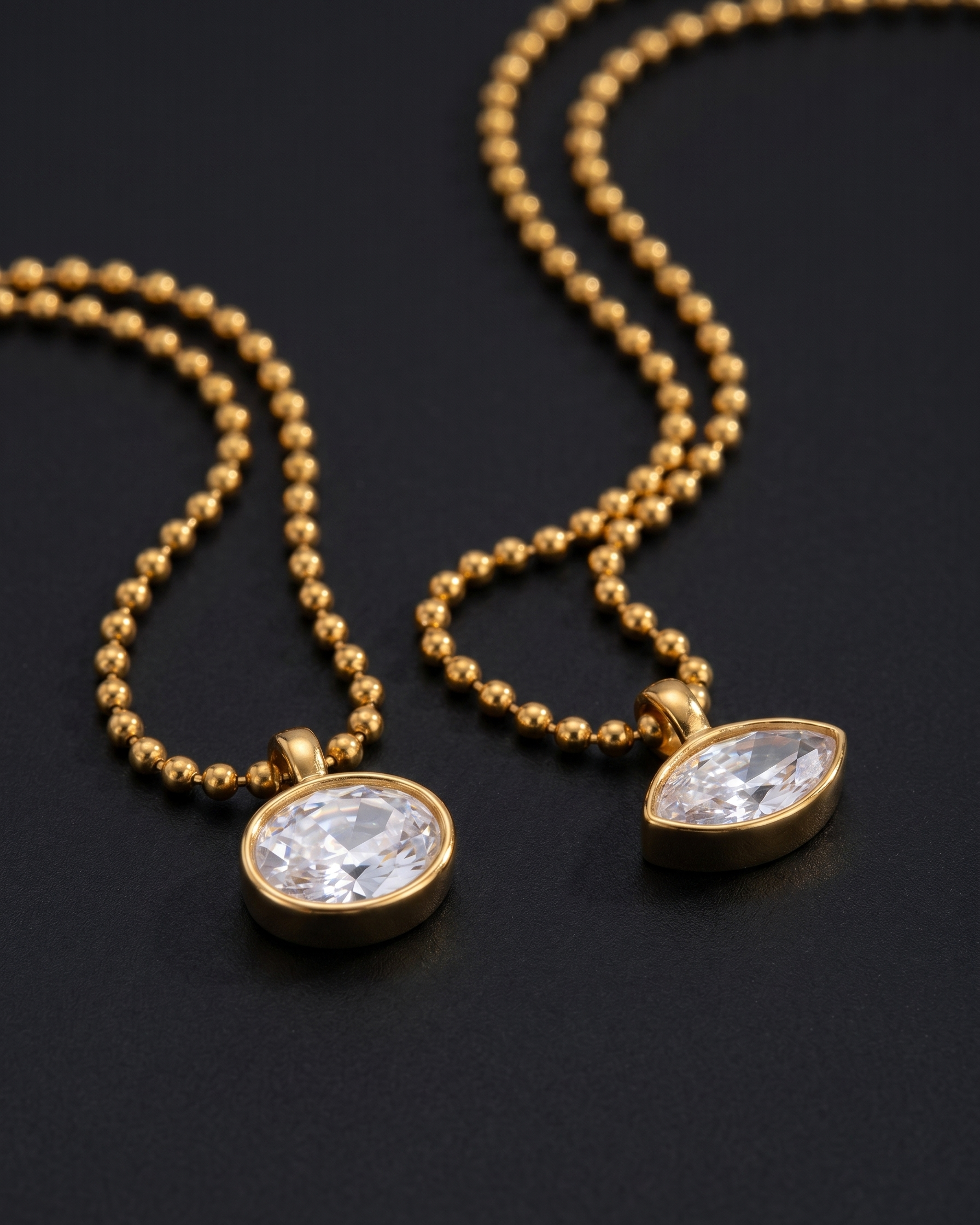 Two gold necklaces with clear gemstones on a black background