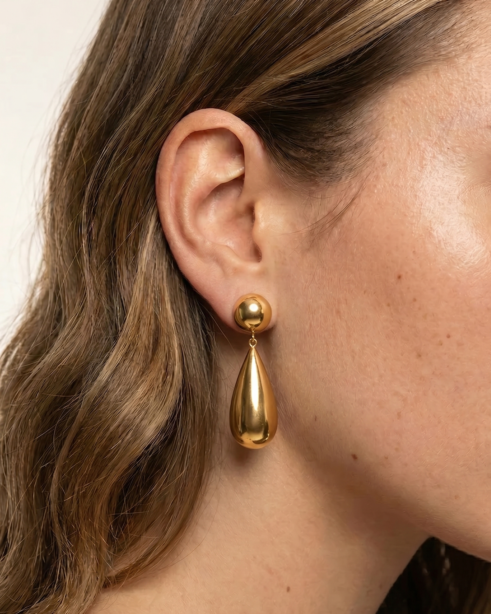 Gold teardrop earring worn by a person with a neutral background