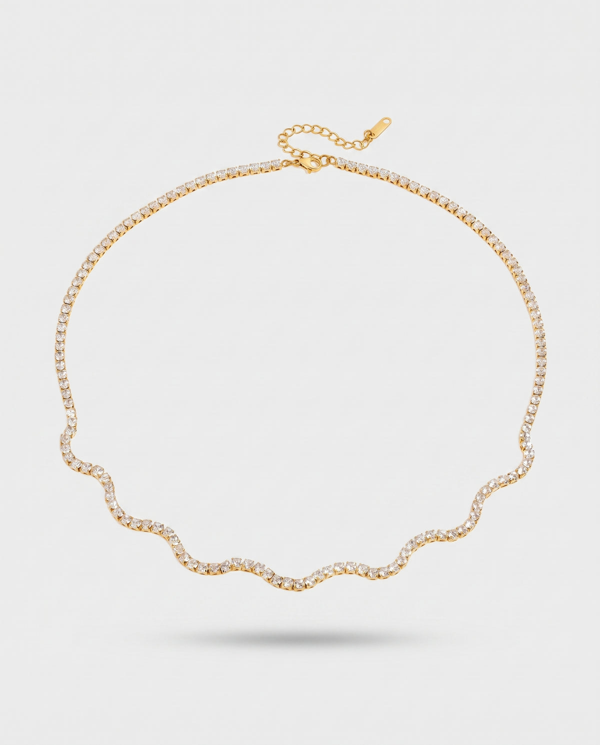 A delicate gold chain necklace with a wavy scalloped edge and pavé-set clear stones, displayed on a light gray background.