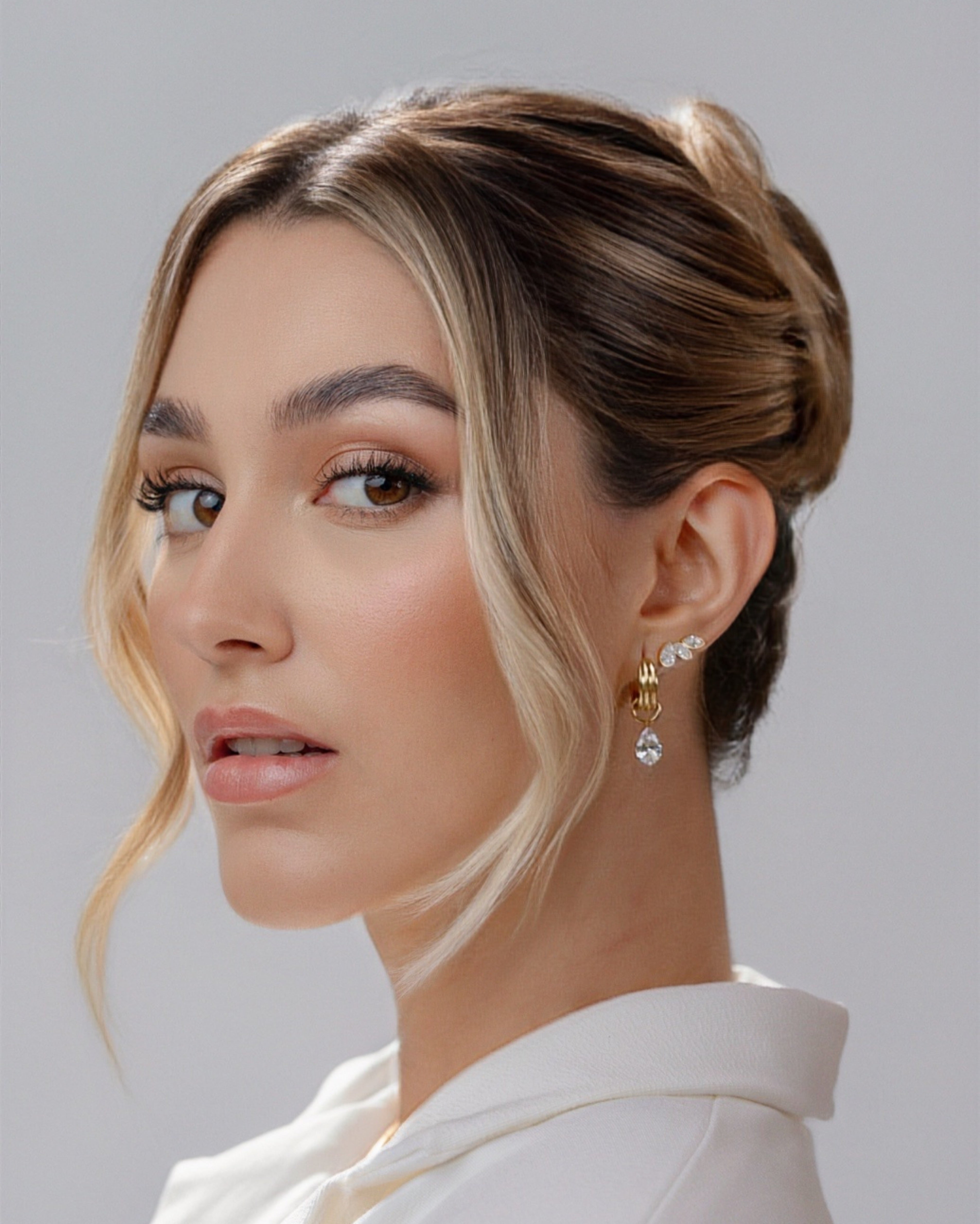 Woman with styled hair and earrings against a neutral background