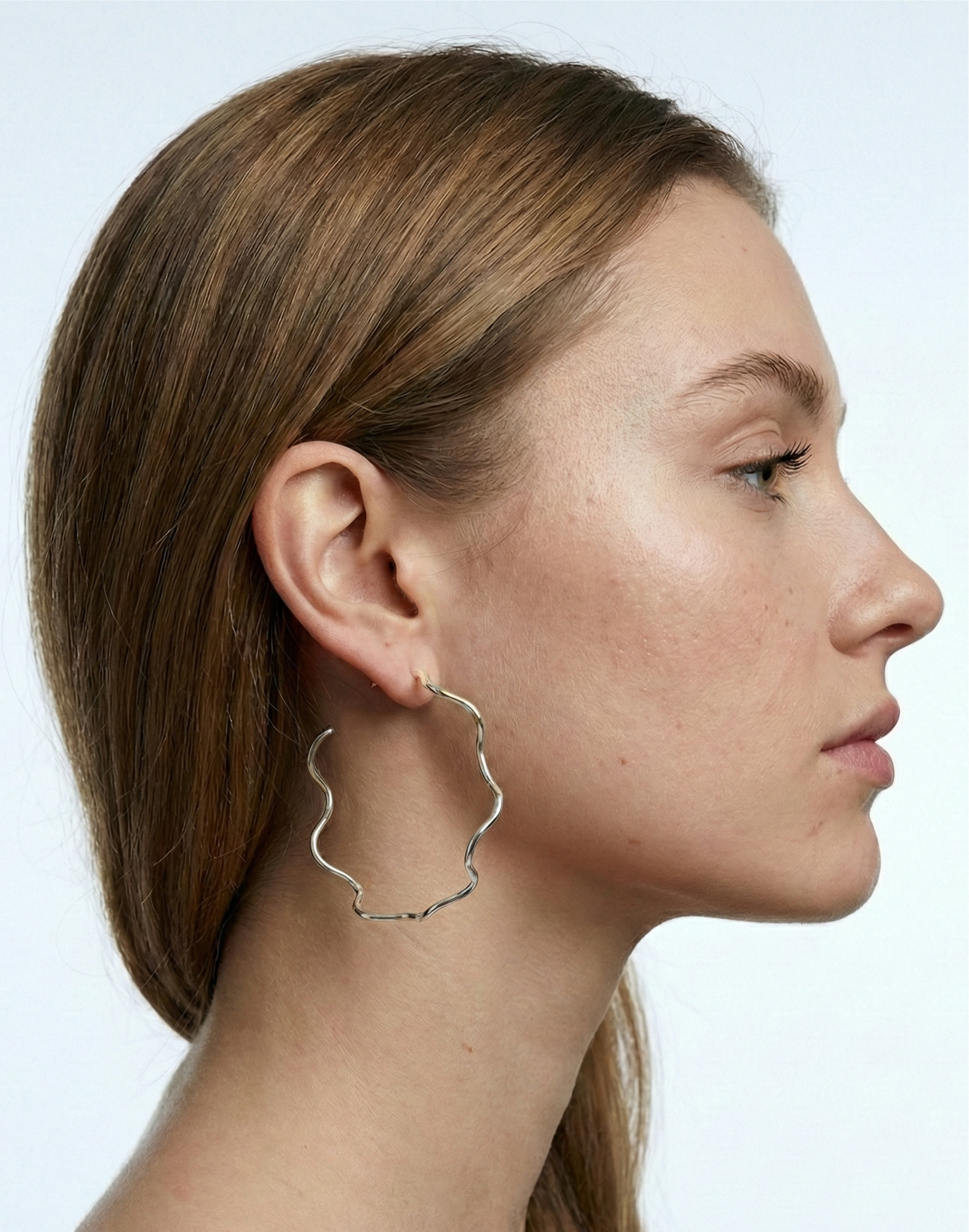 Side profile of a woman wearing silver hoop earrings against a light background