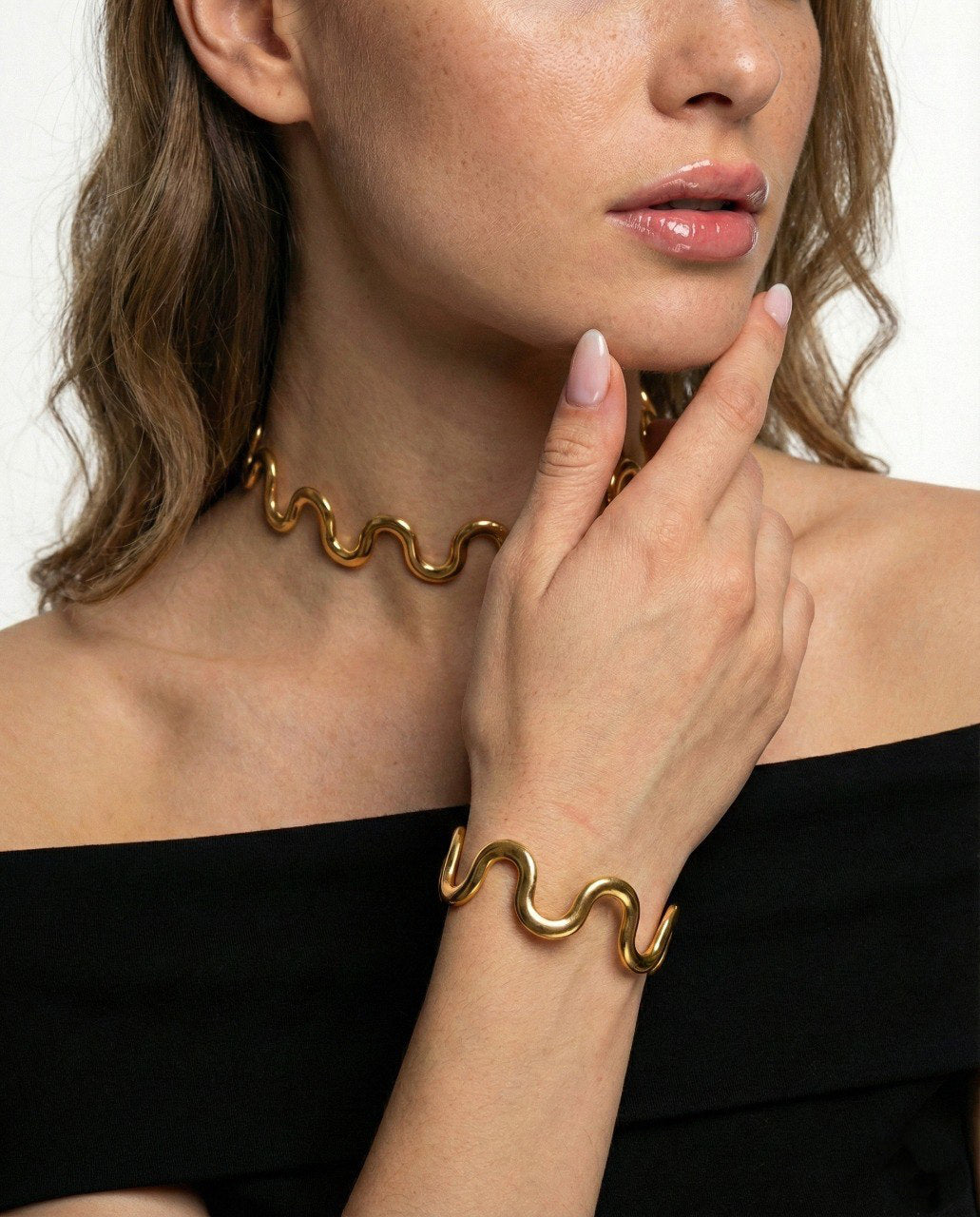 Woman wearing gold wavy necklace and bracelet on a plain background