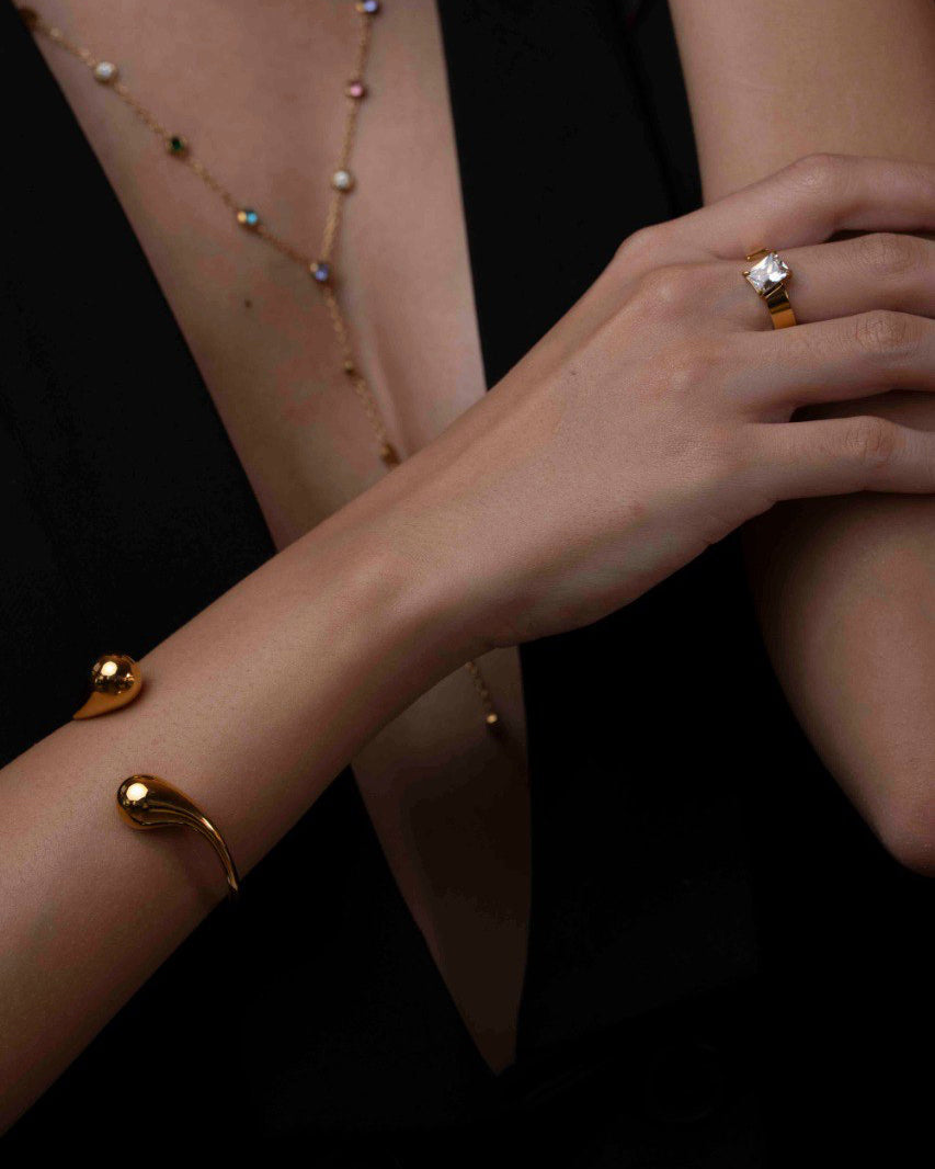 Close-up of a person's arm and hand wearing gold jewelry on a dark background