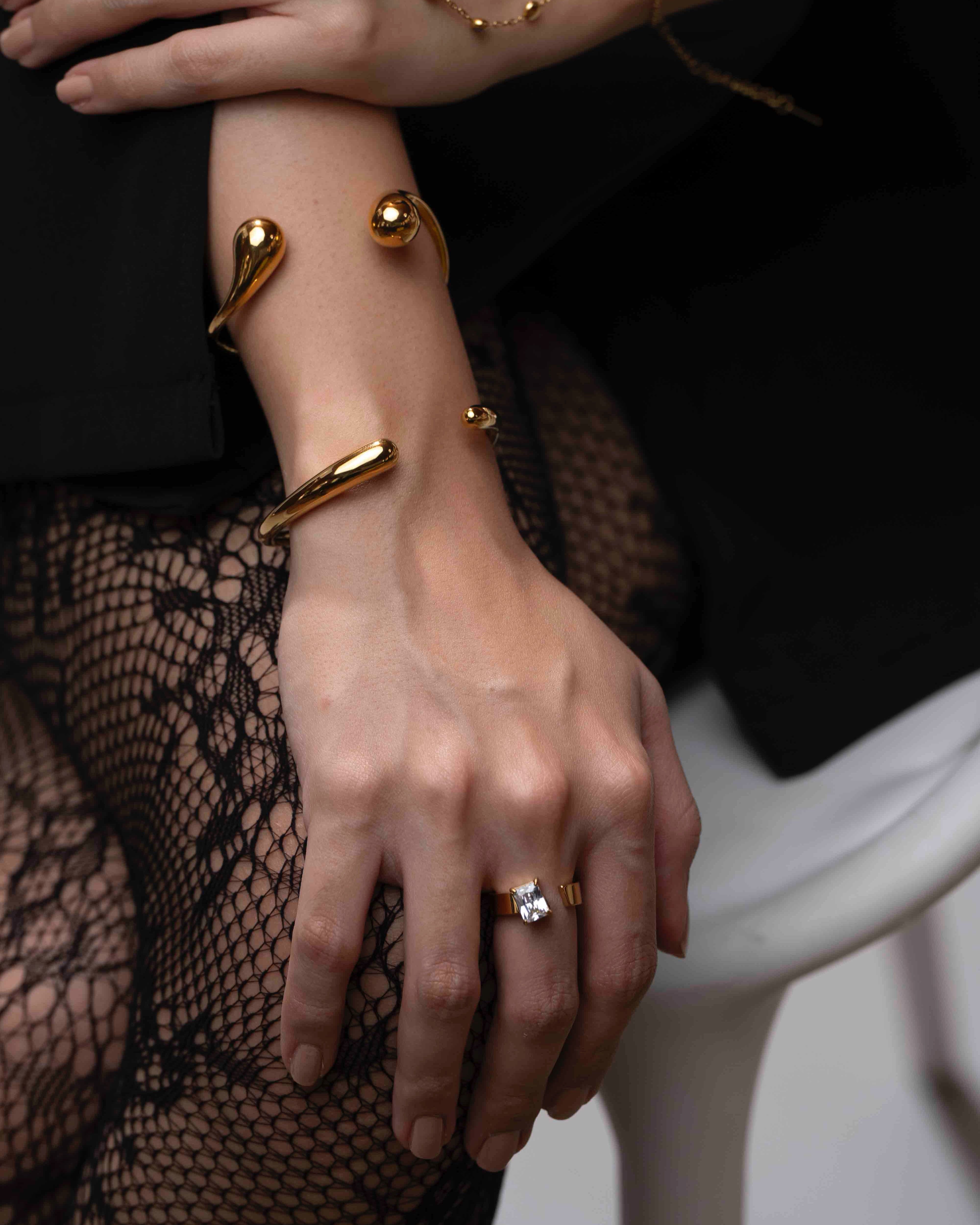 Close-up of a hand wearing gold bracelets and rings on a blurred background