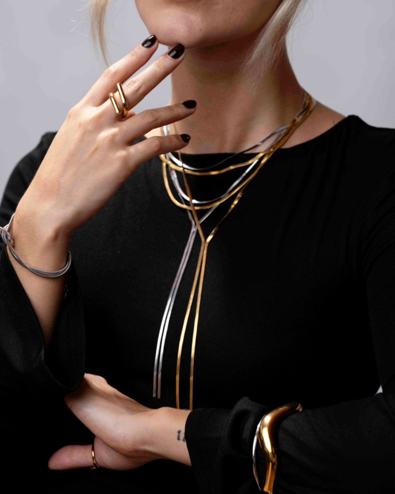 Person wearing a gold necklace and rings with a neutral background