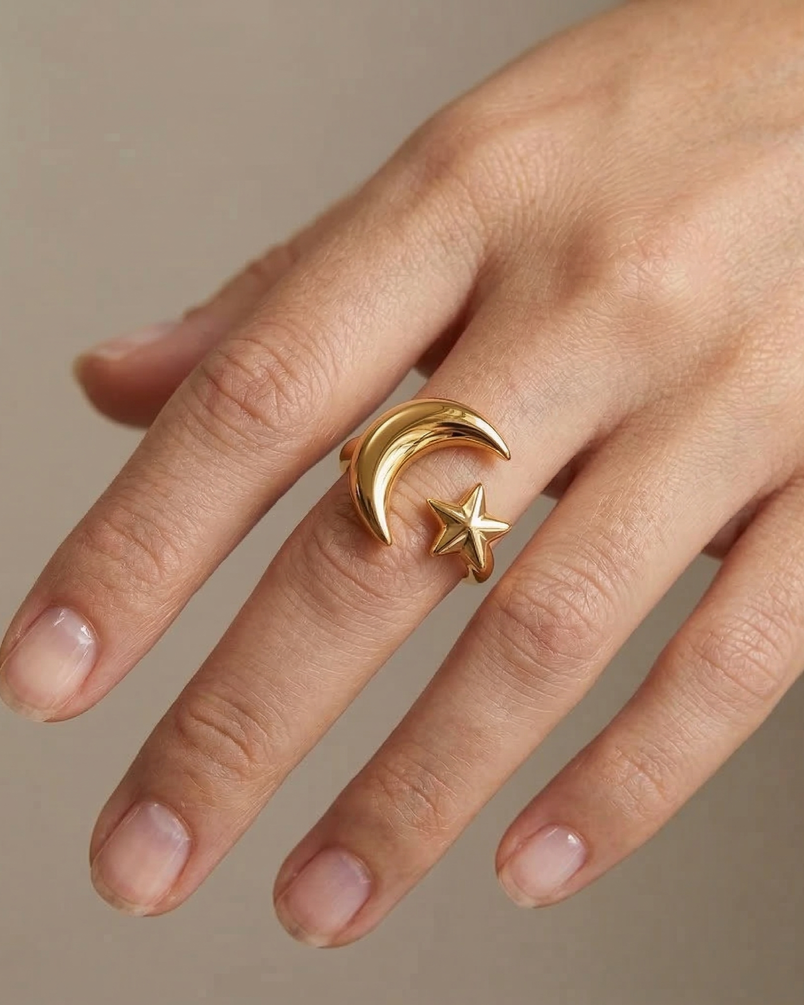 Gold ring with moon and star design on a finger against a neutral background
