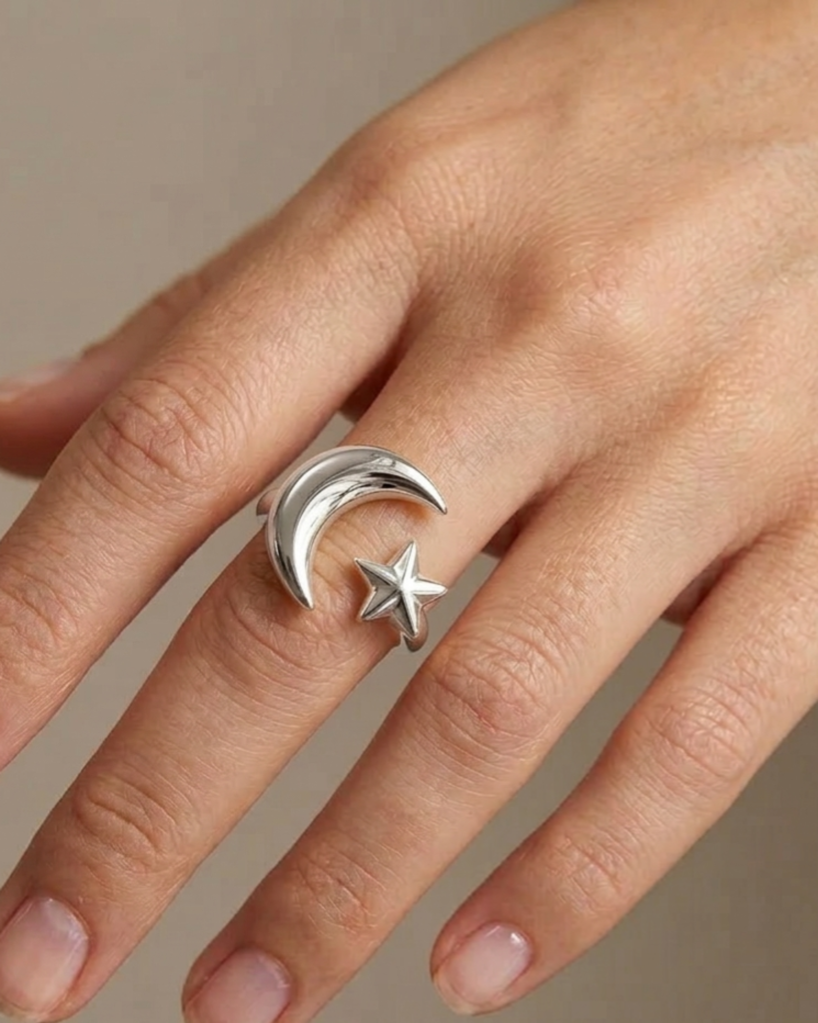 Silver ring with moon and star design on a person's finger against a neutral background