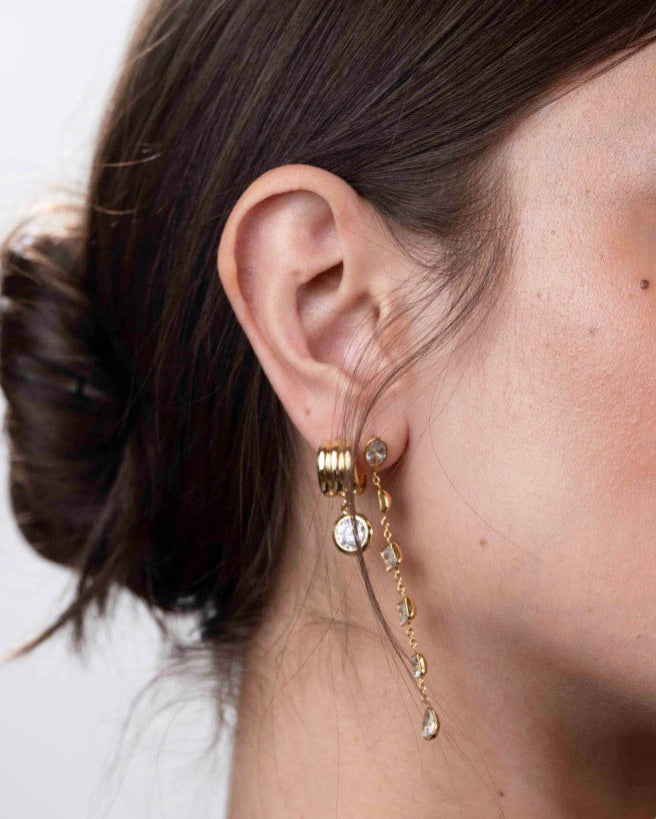Close-up of an ear wearing gold hoop earrings with dangling charms against a neutral background