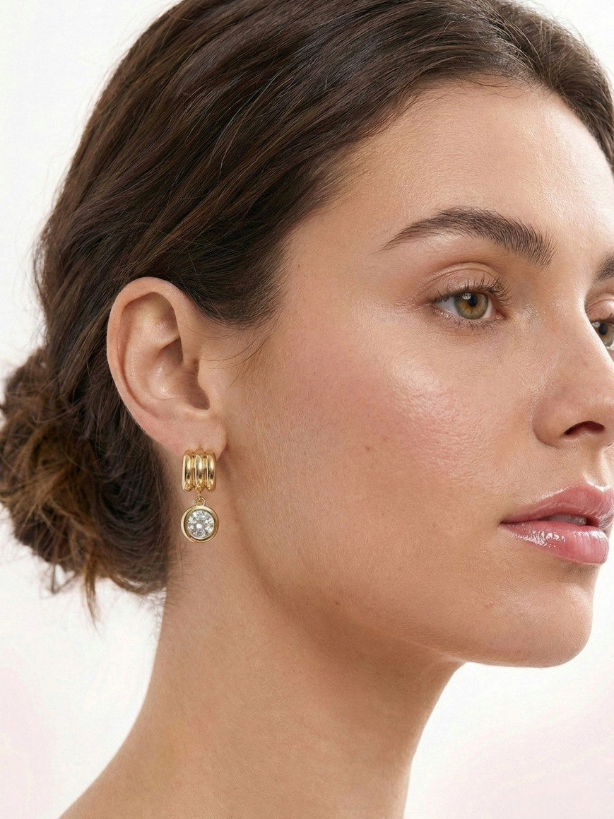 Close-up of a woman wearing gold hoop earrings with a clear gemstone on a white background