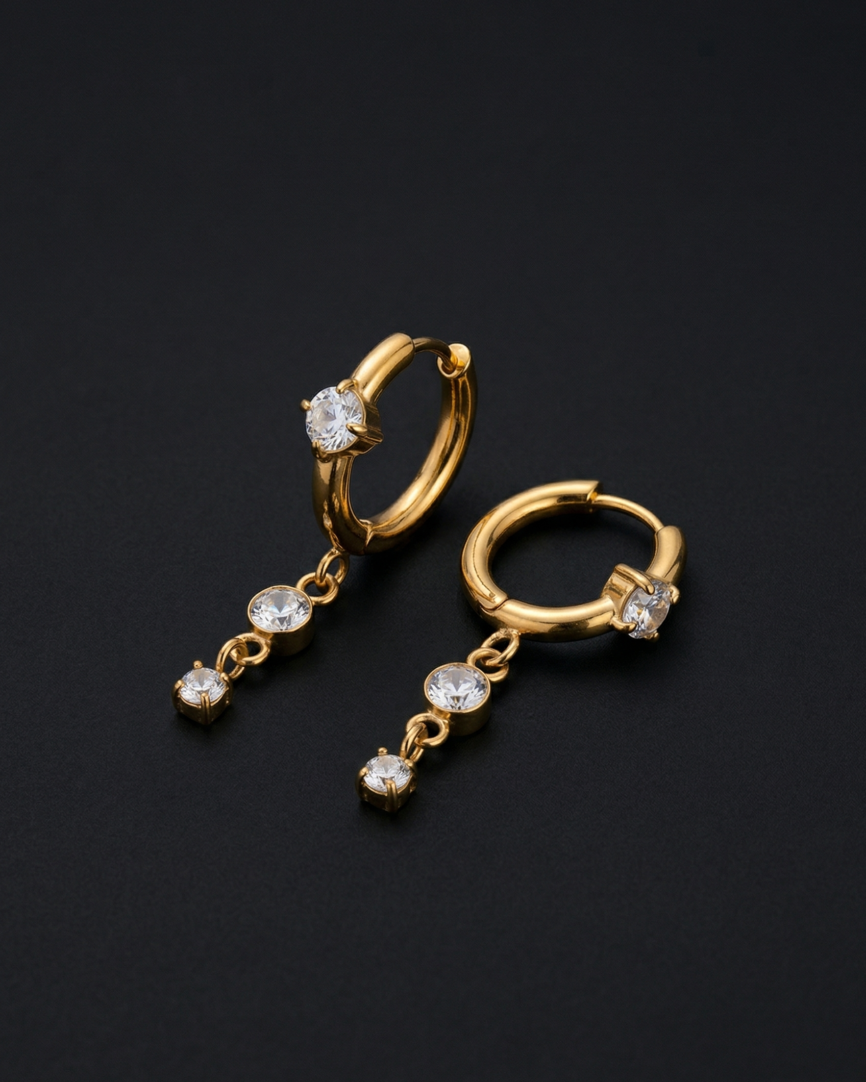 Gold hoop earrings with diamond-like stones on a black background