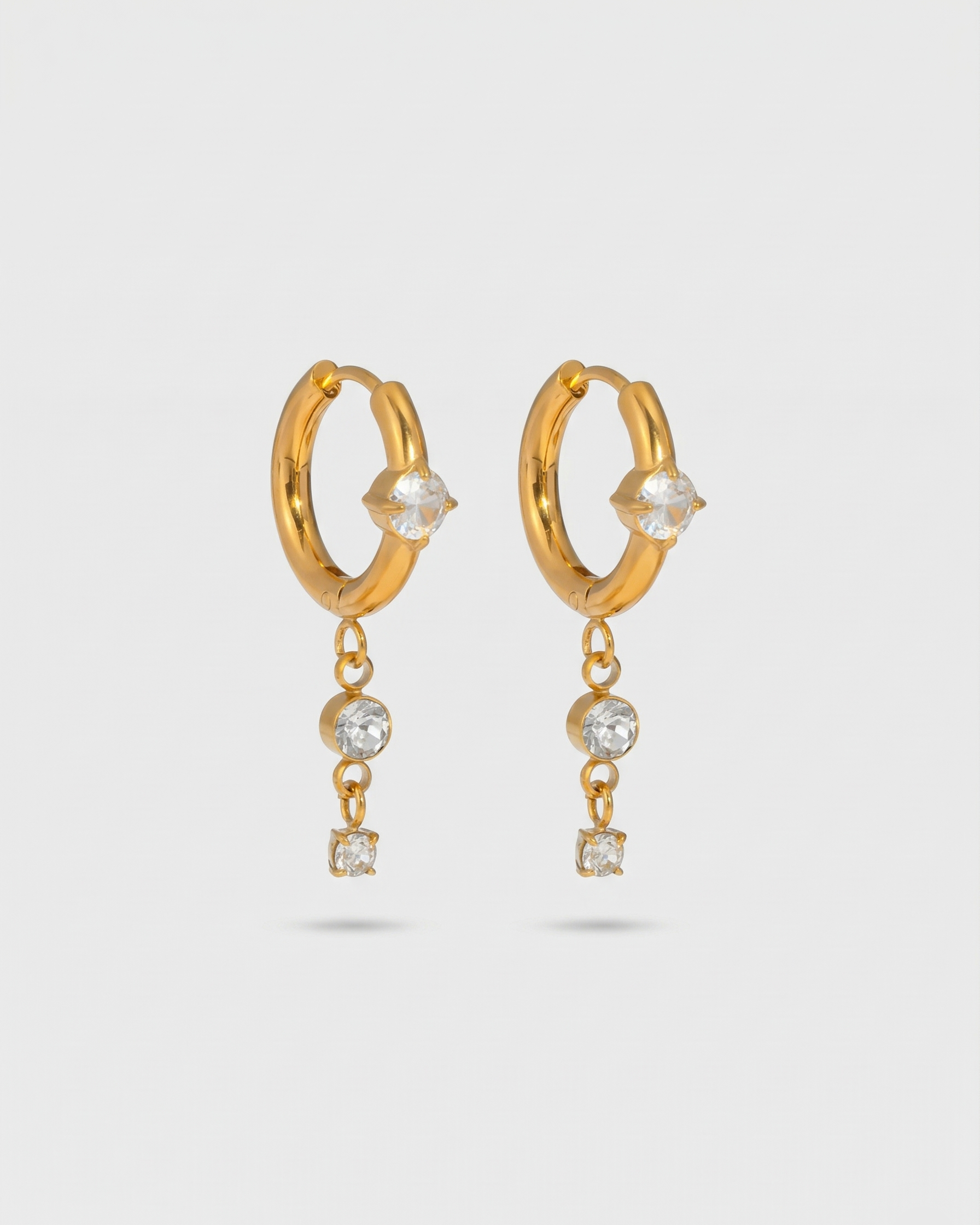 Gold hoop earrings with small crystals on a light gray background