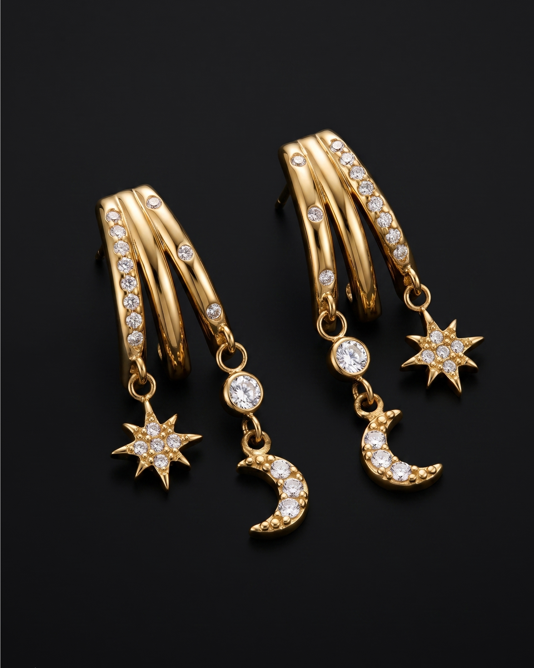 Gold hoop earrings with star and moon charms on a black background