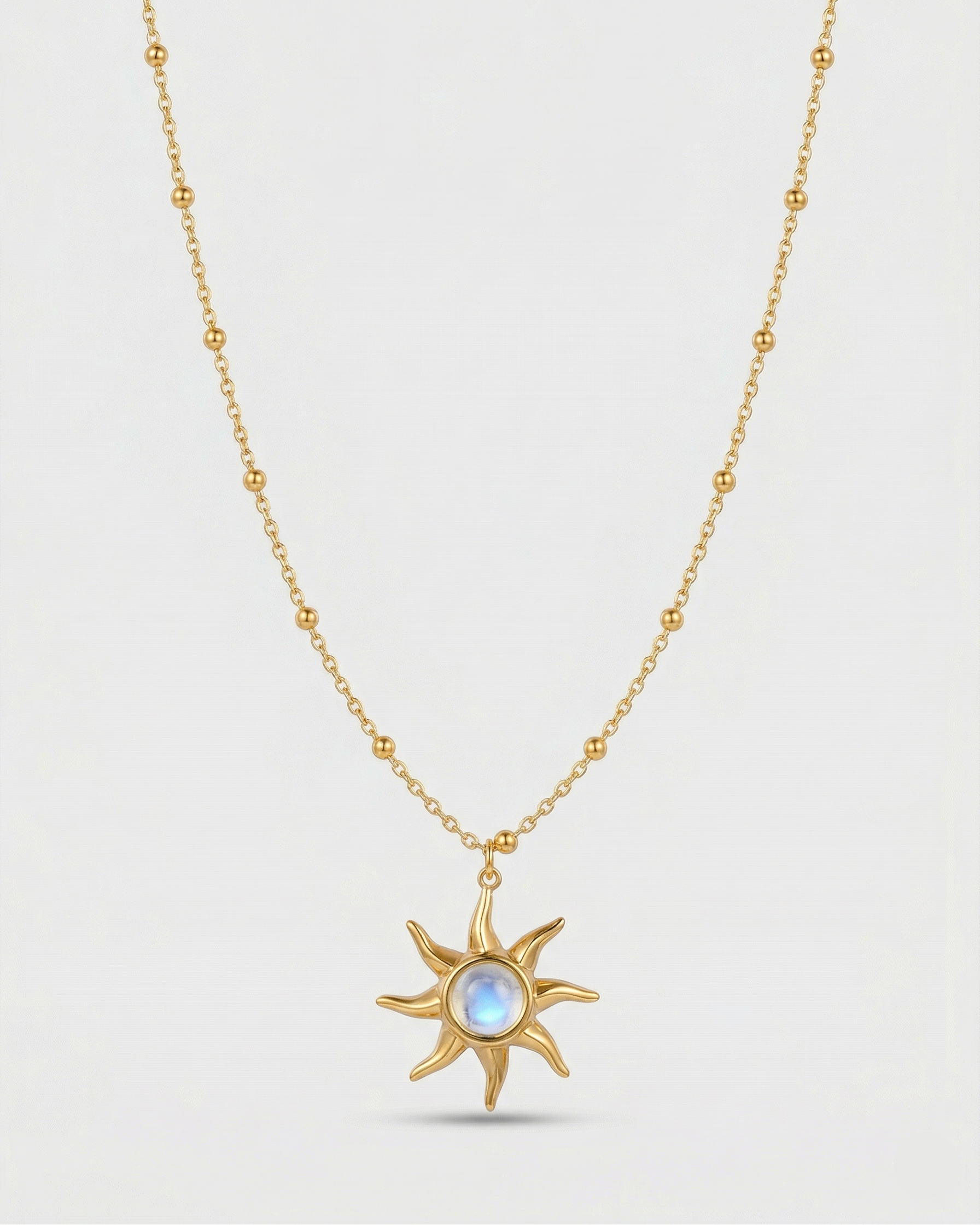 Gold necklace with a sun-shaped pendant on a light gray background