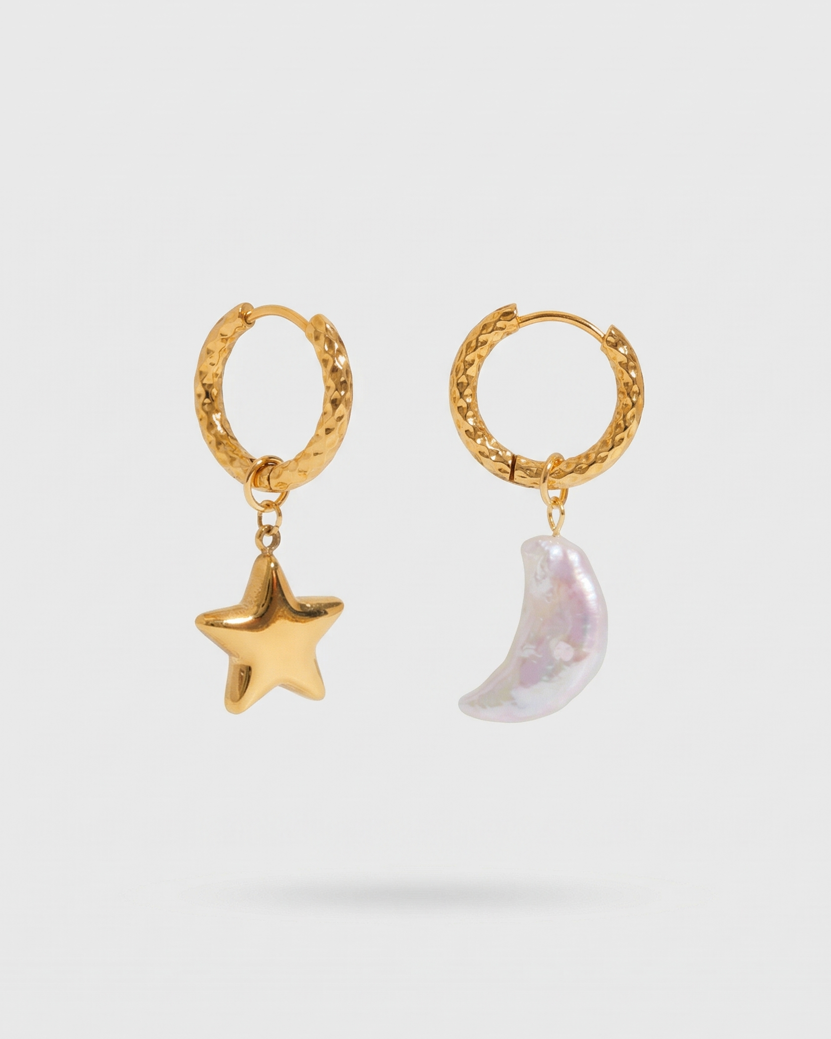 Gold hoop earrings with star and moon charms on a light gray background