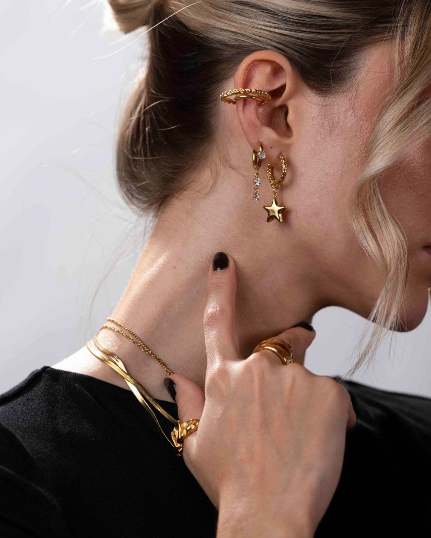 Close-up of a person wearing gold earrings and necklaces against a light background
