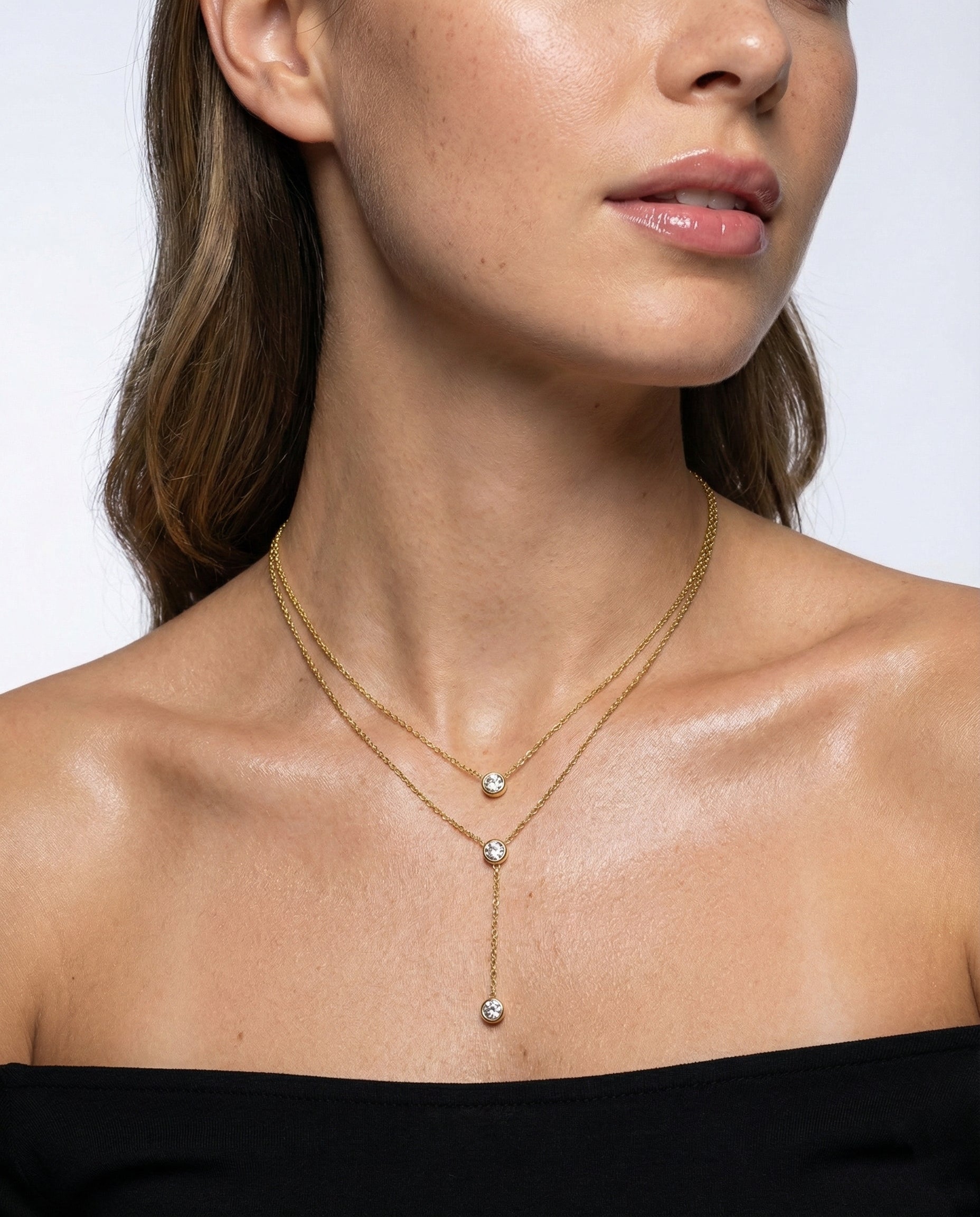Woman wearing a gold necklace with three diamond pendants on a plain background