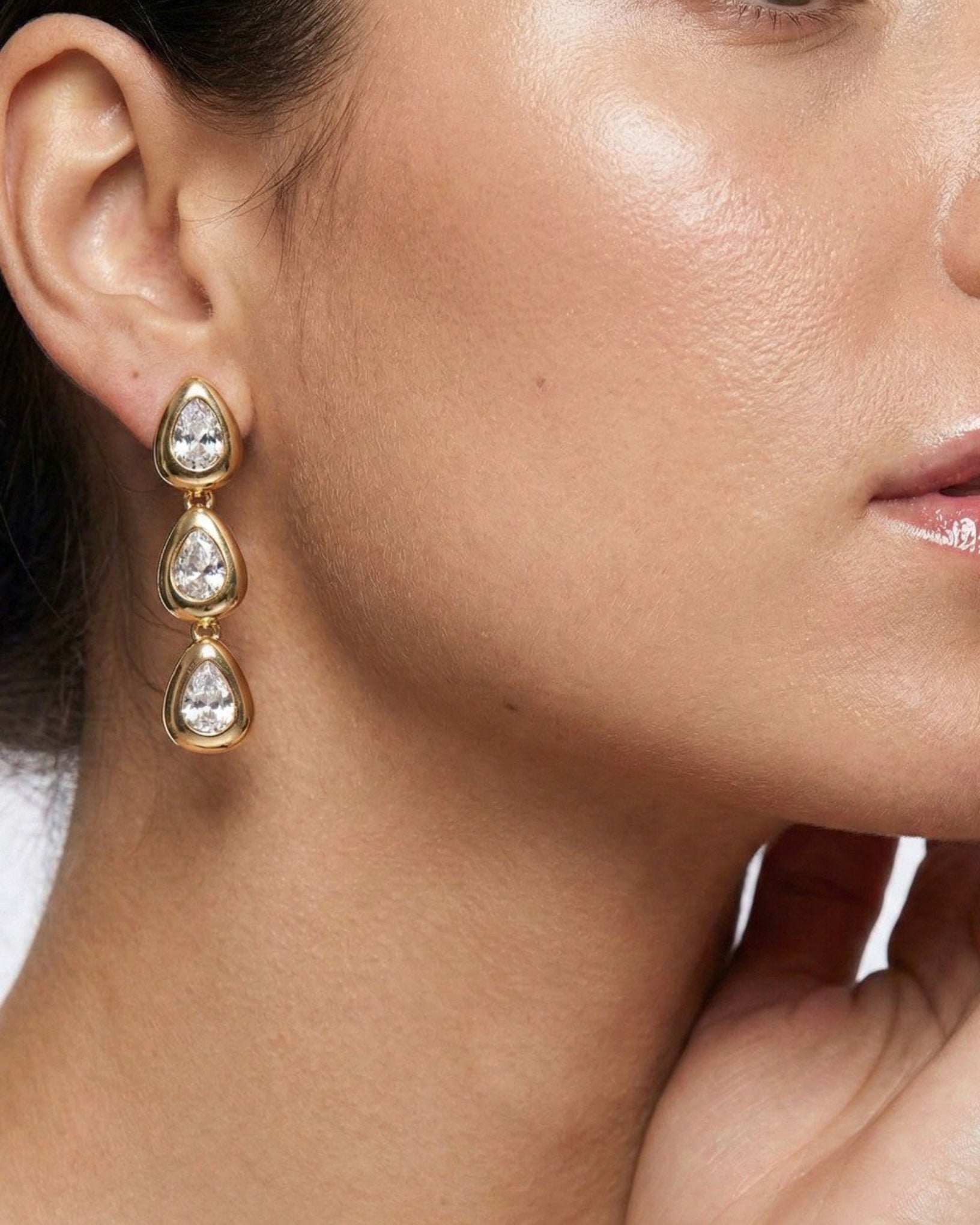 Close-up of a woman wearing gold teardrop earrings.