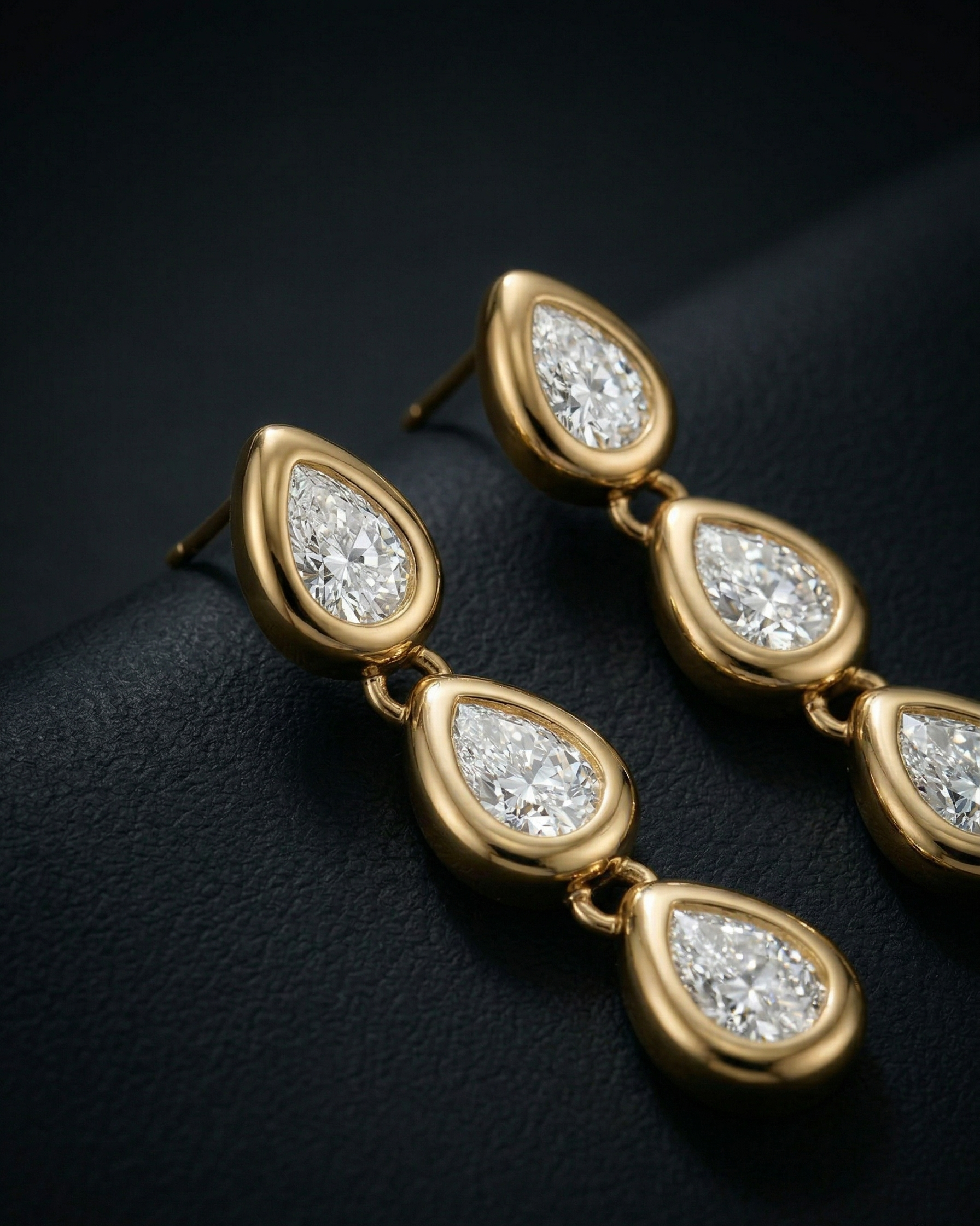 Gold earrings with teardrop-shaped diamonds on a dark background
