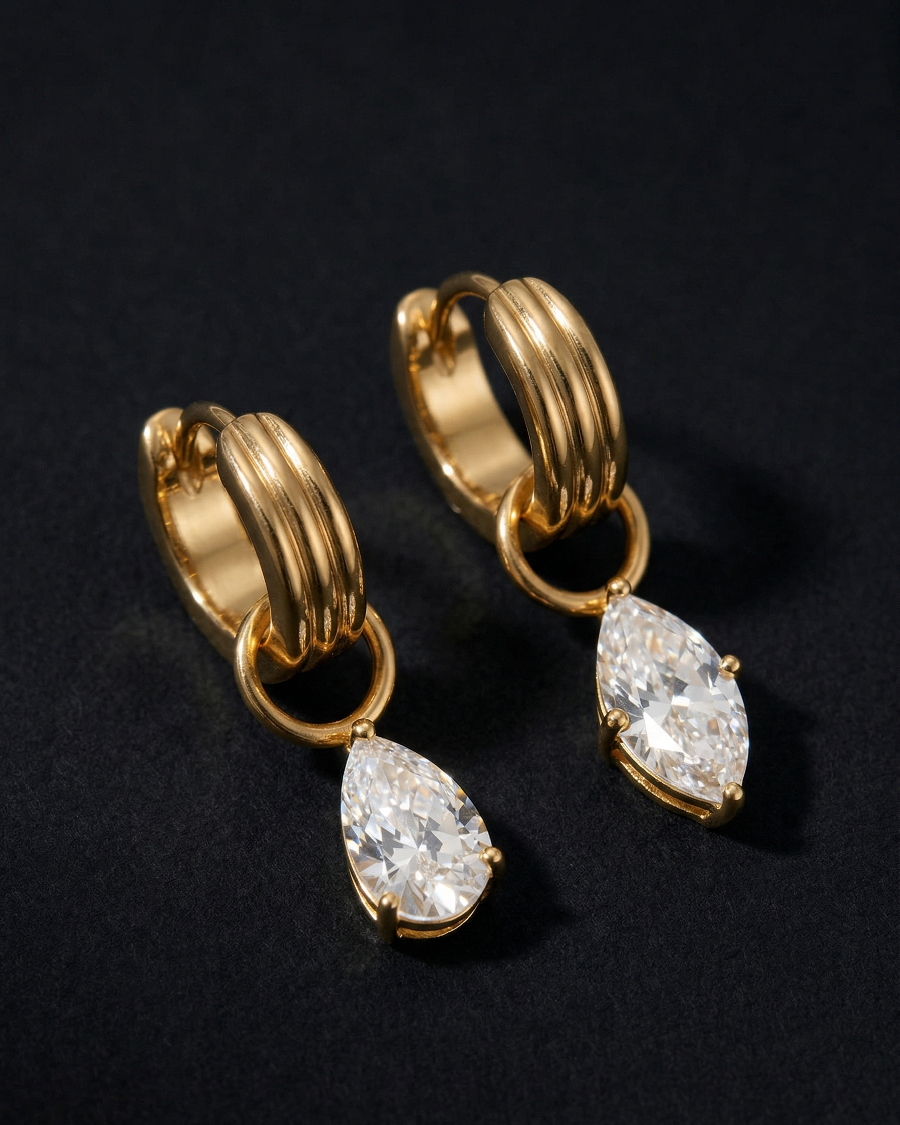 Gold hoop earrings with teardrop-shaped gemstones on a black background