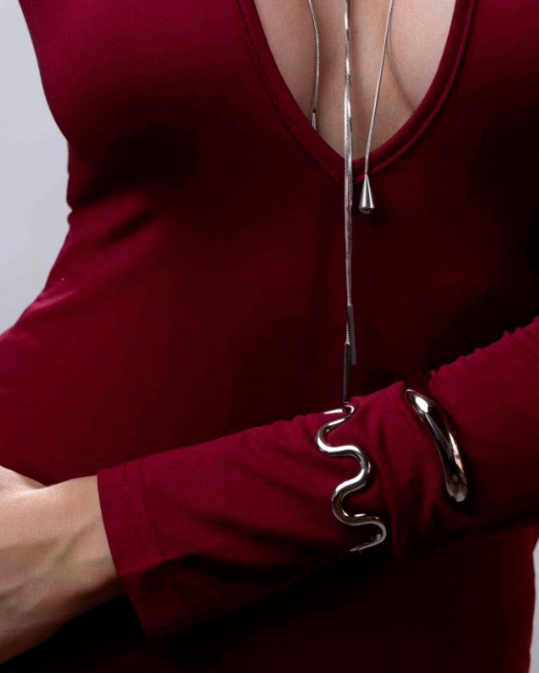 Person wearing a deep neckline dress with a silver necklace and bracelet on a plain background