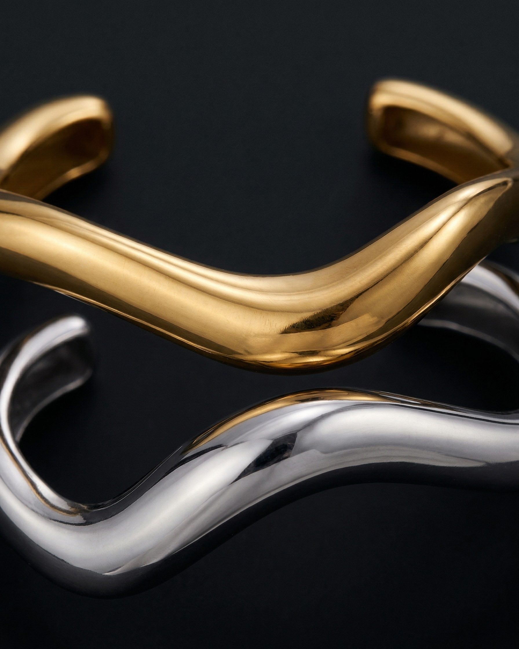 Gold and silver twisted cuff bracelets on a black background