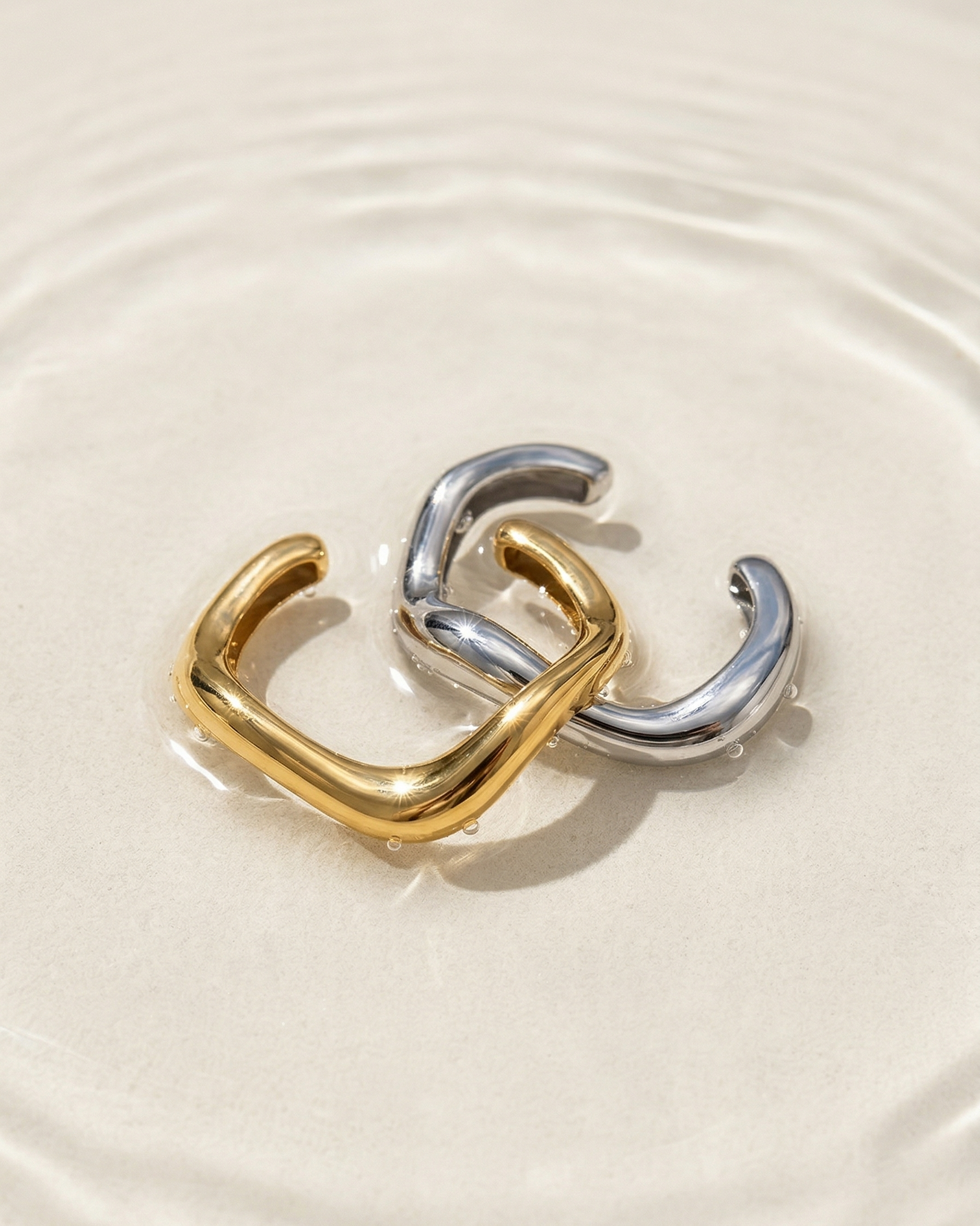 Two gold and silver hoop earrings on a white surface with water ripples.