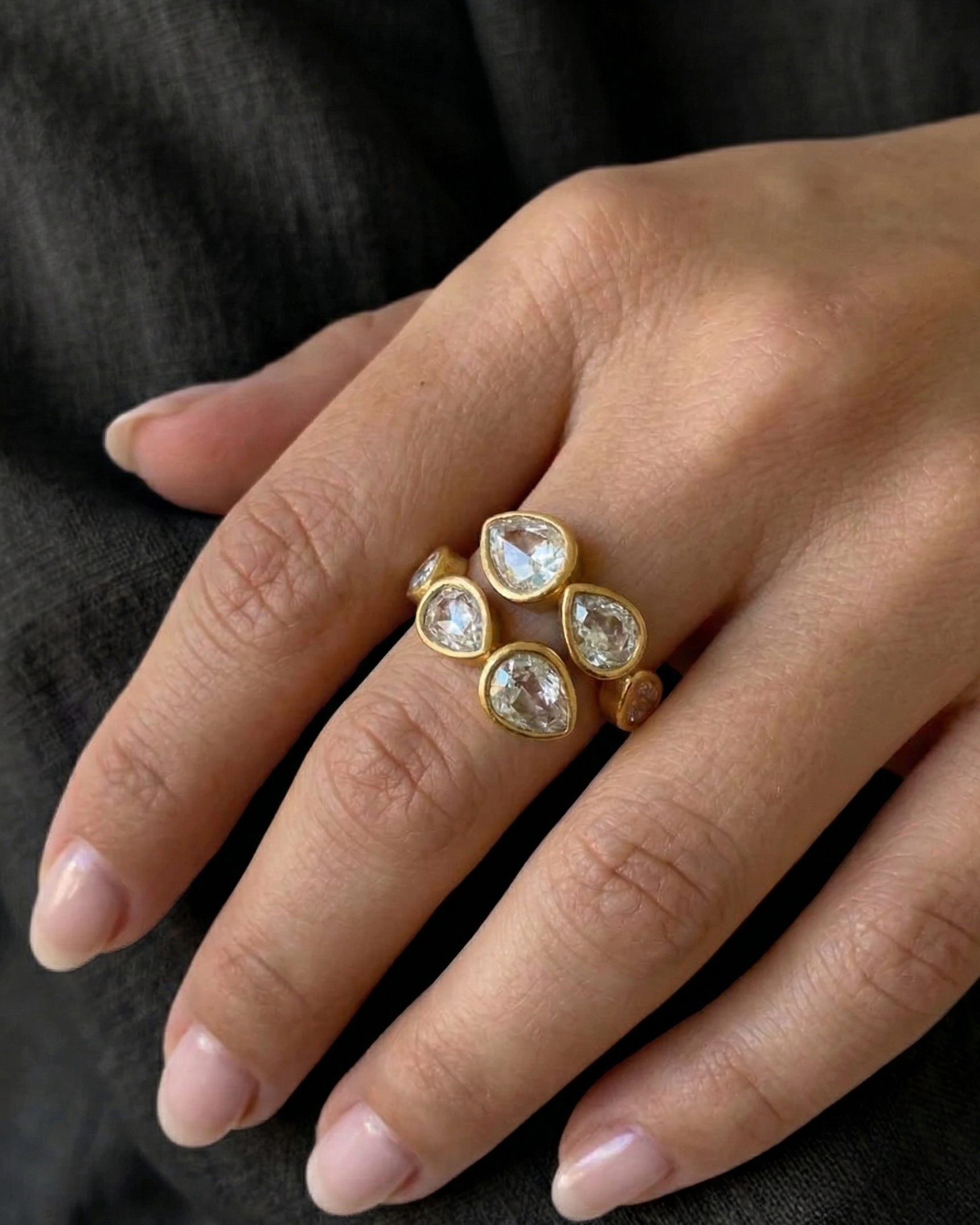 Gold ring with clear gemstones on a hand against a dark background